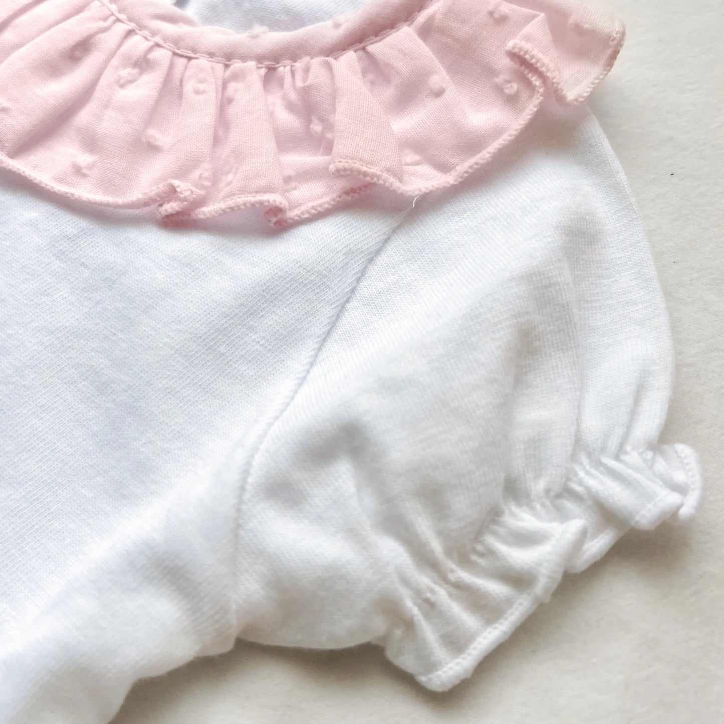 Detalle de conjunto de niña de blusa con volante en el cuello y cubrepañal rosa