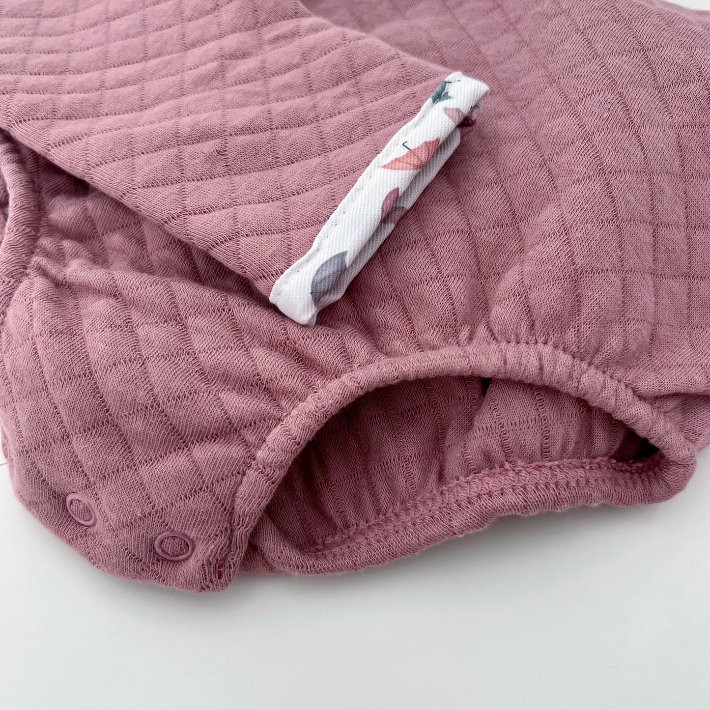 Detalle de pelele de niña con cuello redondo en contraste rosa