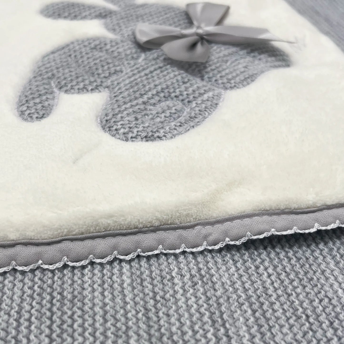 Detalle de manta con motivo de conejos de punto y lazo gris
