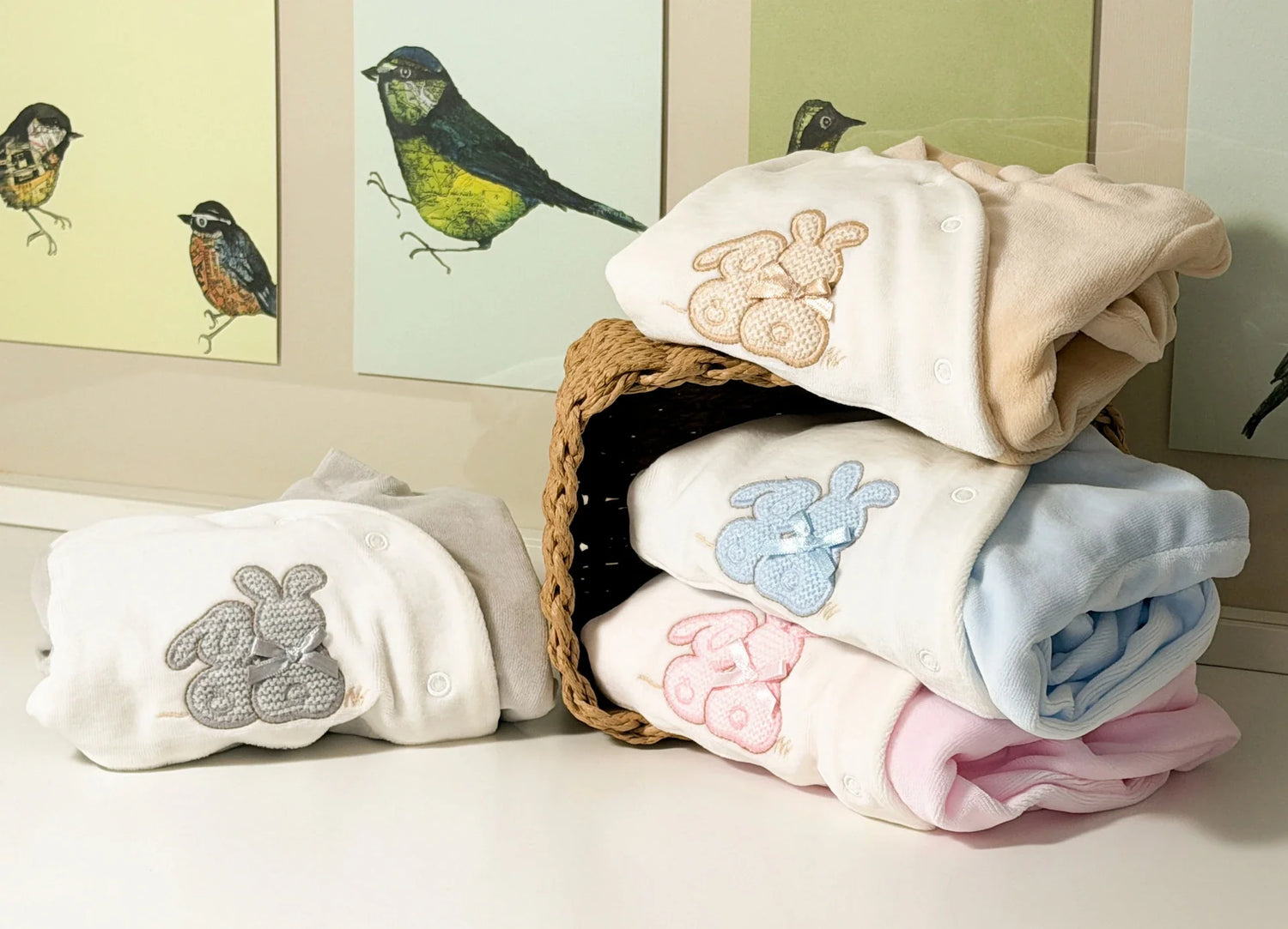 Cuatro variantes de pelele con motivo de conejos de punto y lazo en los colores gris, beige, azul y rosa apilados