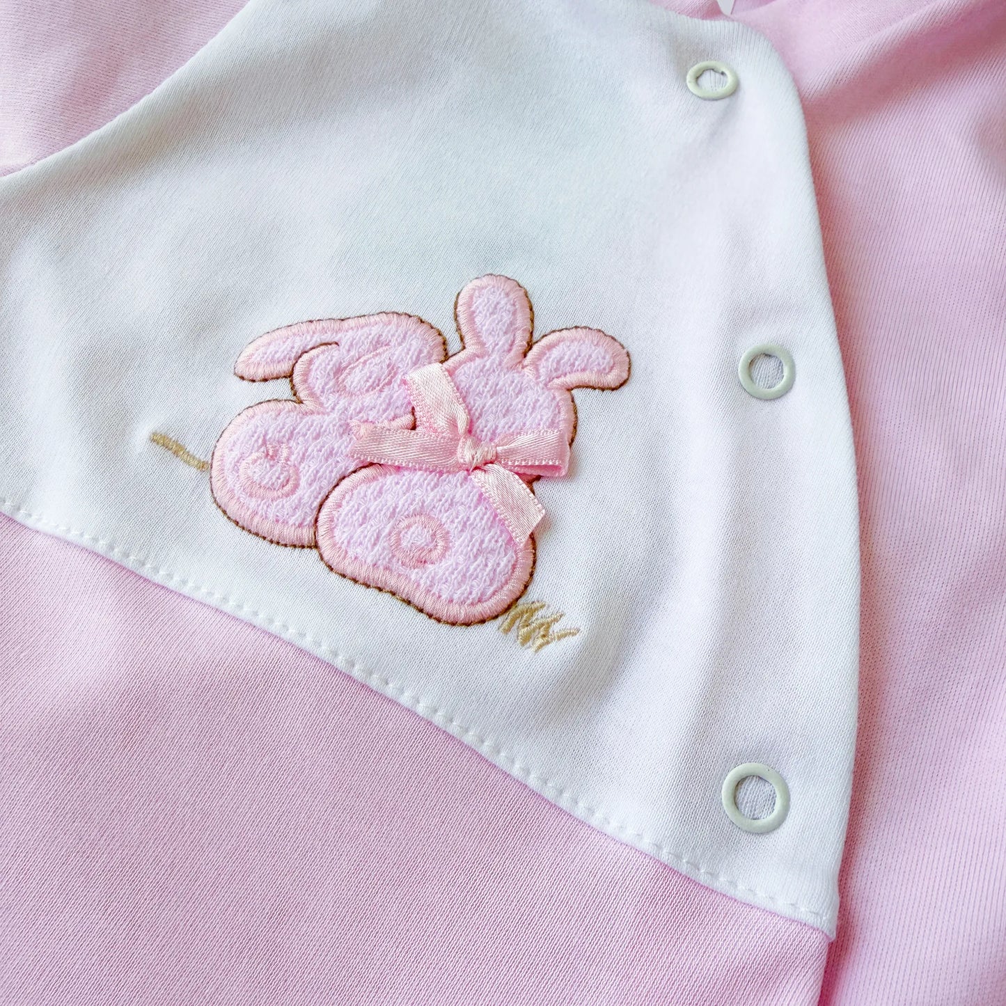 Detalle de pelele de algodón con motivo de conejos de punto y lacito rosa
