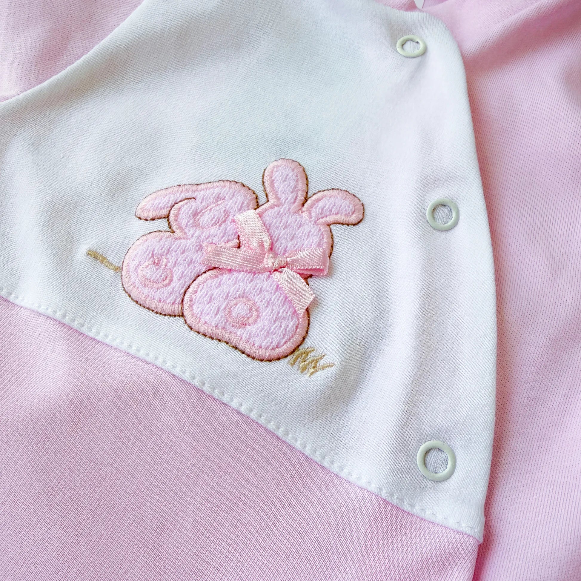 Detalle de pelele de algodón con motivo de conejos de punto y lacito rosa