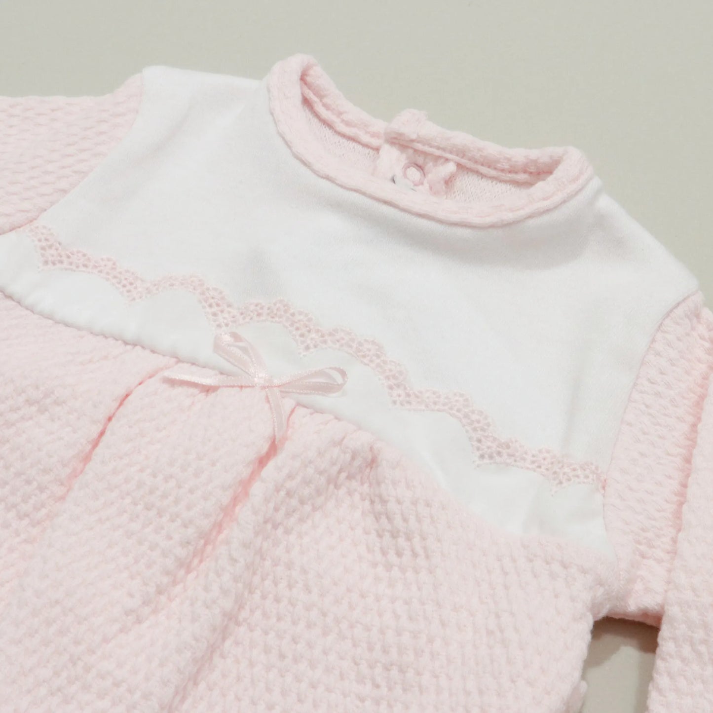 Detalle de pelele con efecto encaje y lazito en el pecho rosa