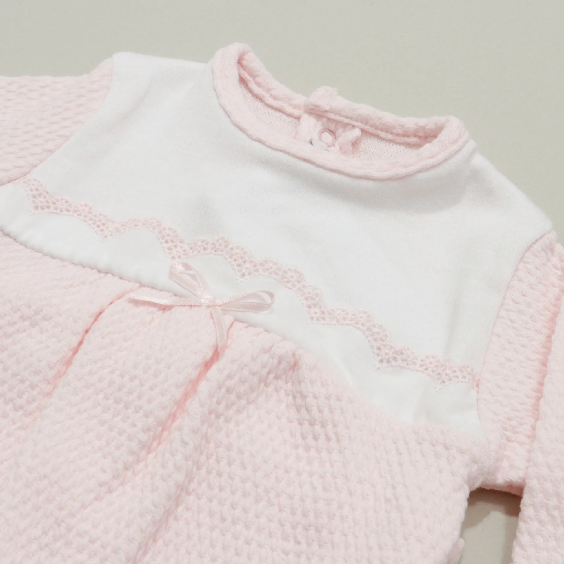 Detalle de pelele con efecto encaje y lazito en el pecho rosa