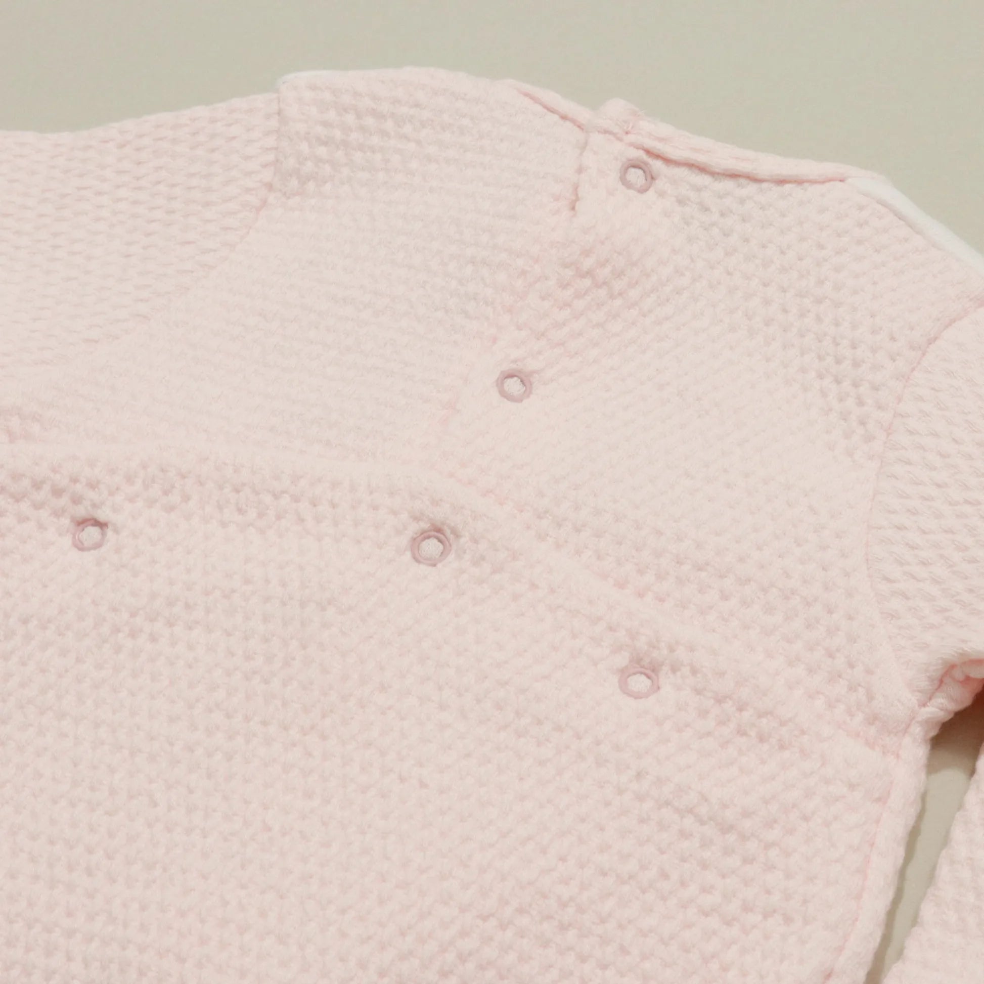 Detalle de pelele con efecto encaje y lazito en el pecho rosa