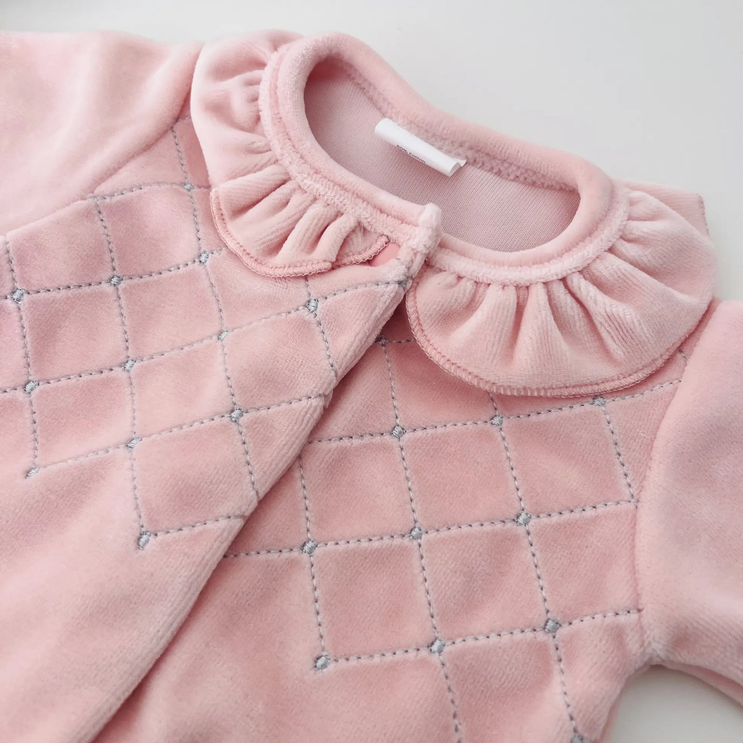 Detalle de pelele de niña con cuello redondo y bordado de rombos rosa
