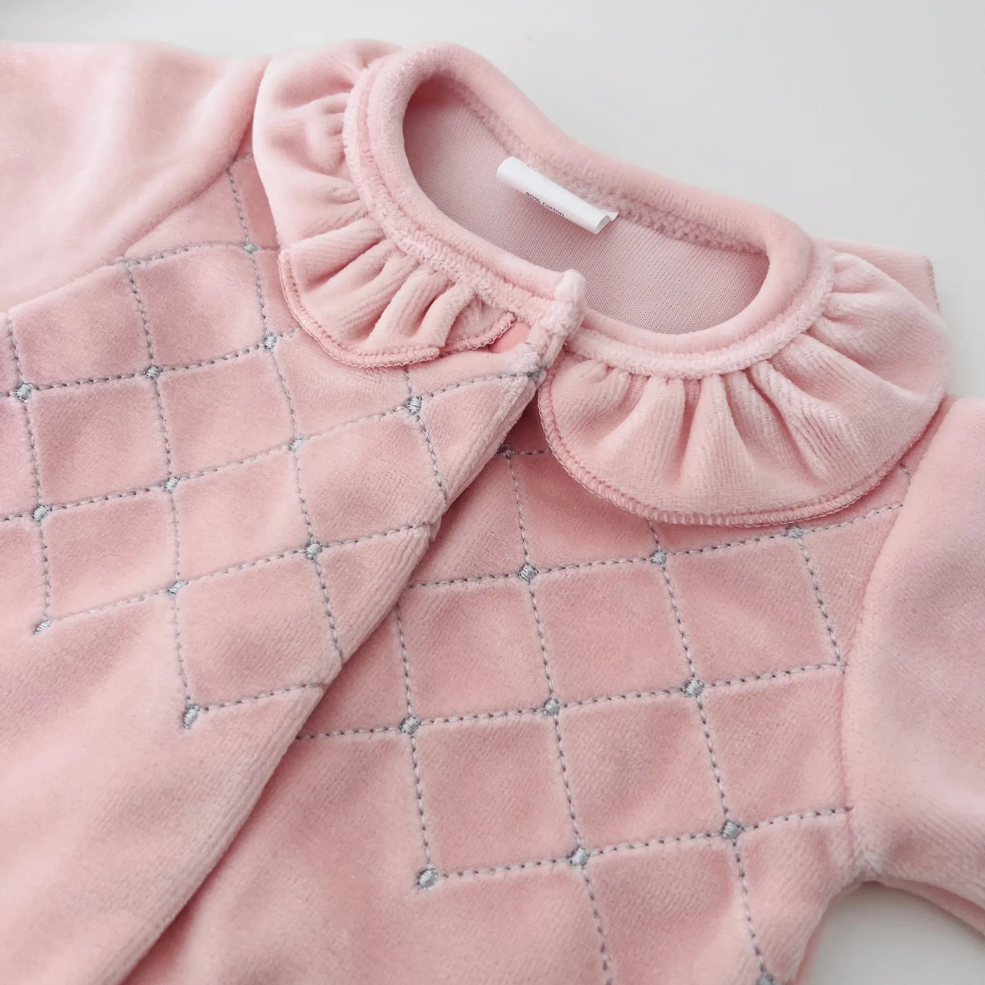 Detalle de pelele de niña con cuello redondo y bordado de rombos rosa