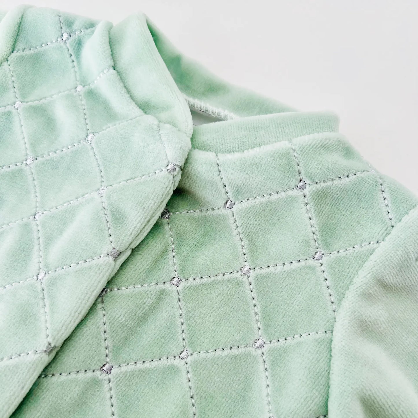 Detalle de pelele de niño con bordado de rombos verde