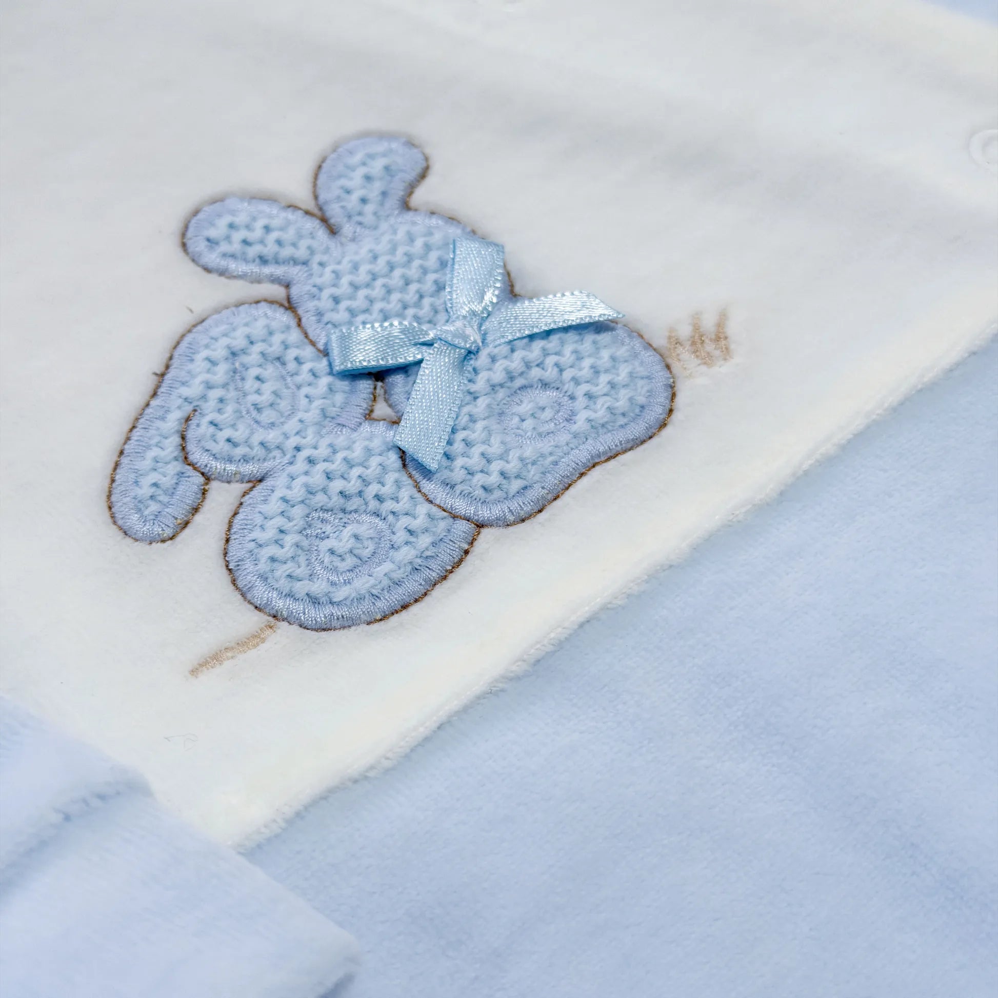 Detalle de pelele con motivo de conejos de punto y lazito azul