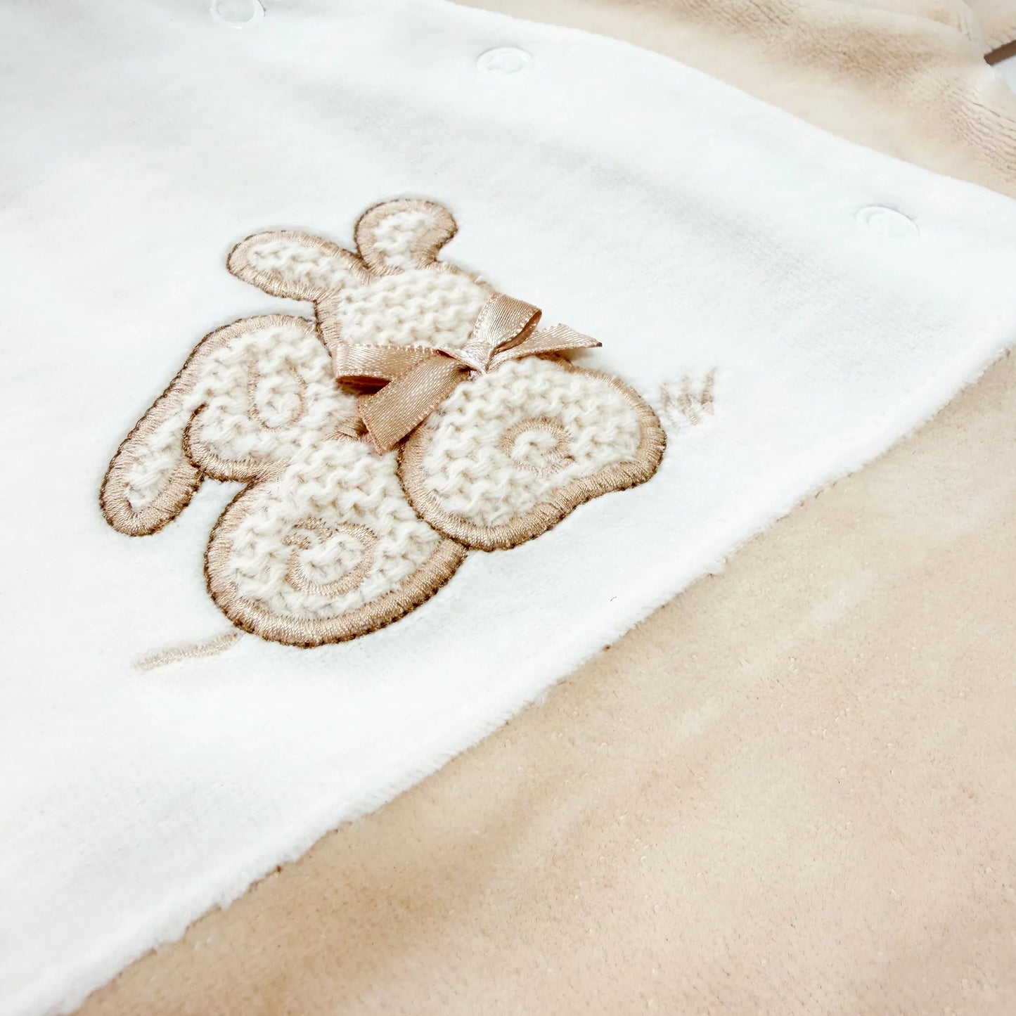Detalle de pelele con motivo de conejos de punto y lazito beige