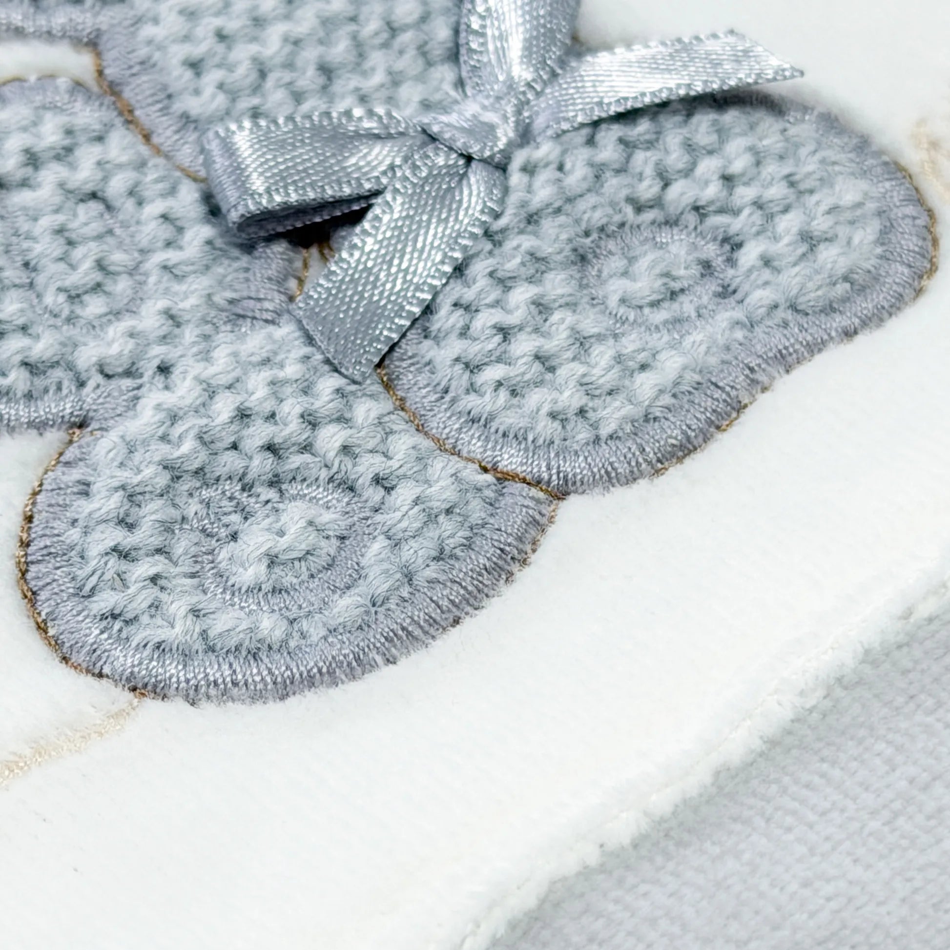 Detalle de pelele con motivo de conejos de punto y lazito gris