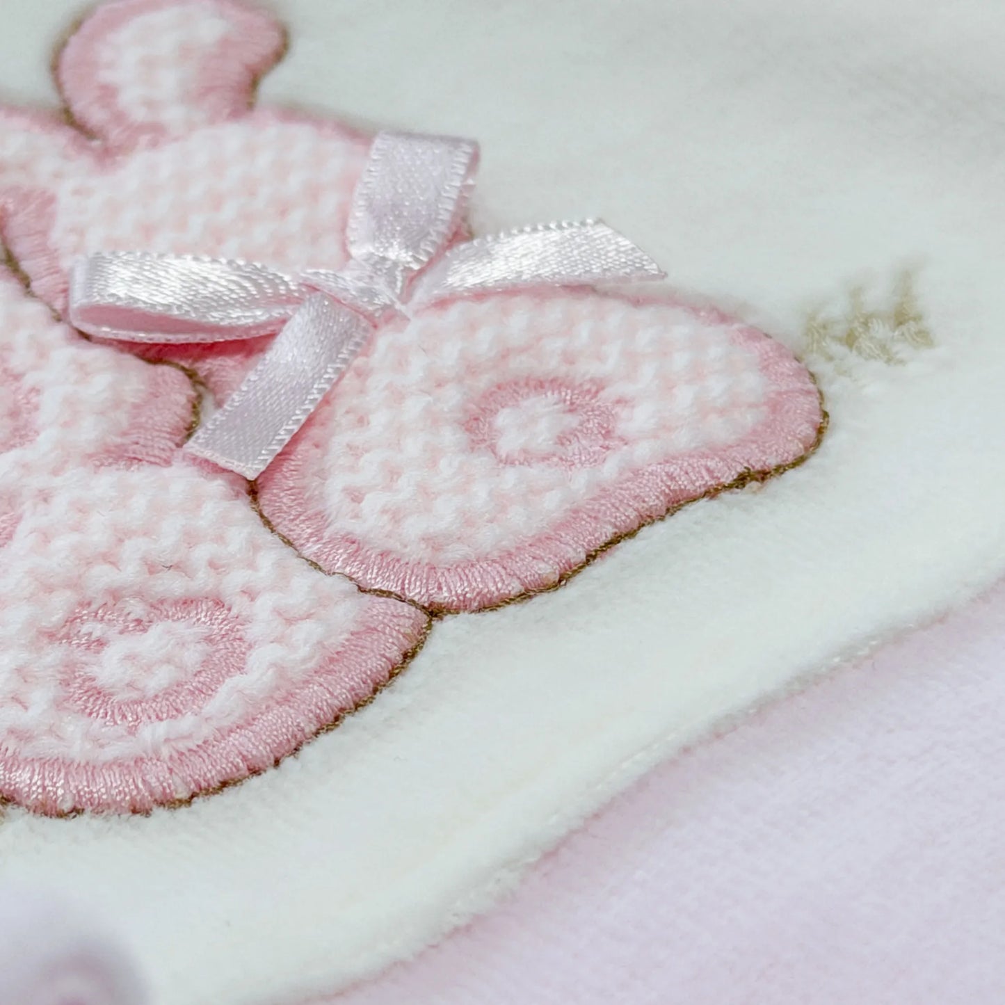 Detalle de pelele con motivo de conejos de punto y lazito rosa