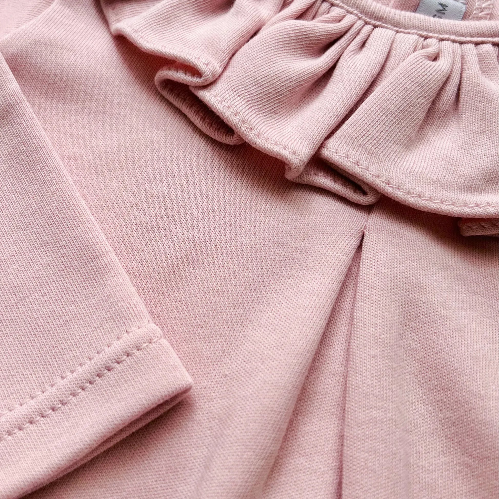 Detalle de camisa de niña con volante en el cuello y pliegue delantero rosa
