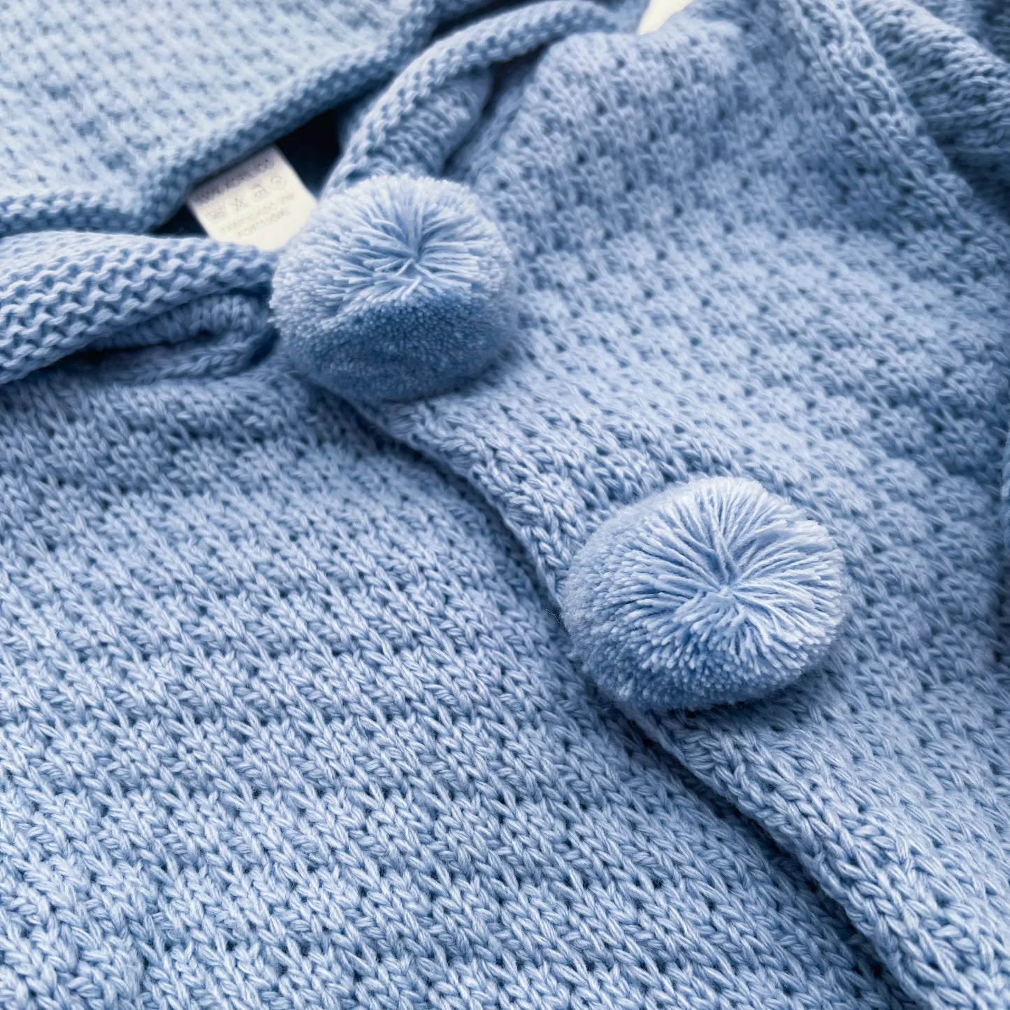 Detalle de chaqueta de punto con capucha y pompones en la zona de los botones azul