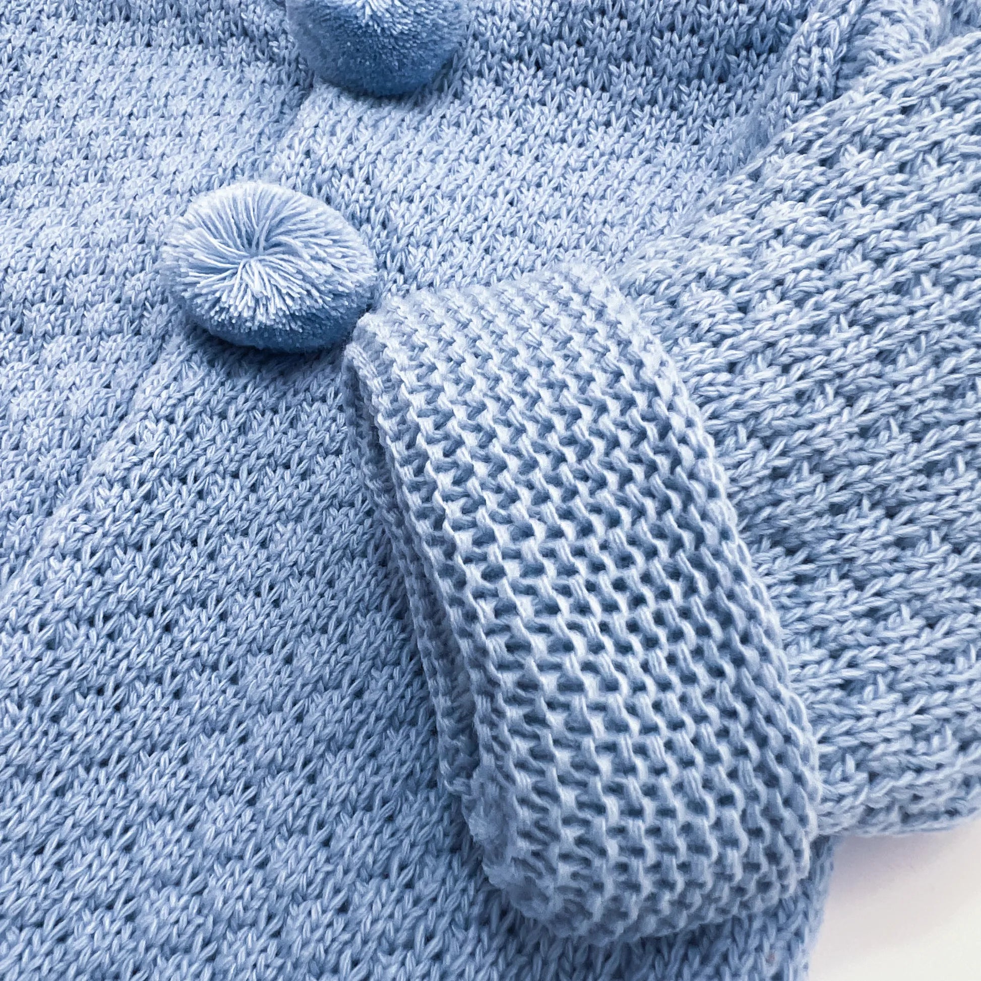 Detalle de chaqueta de punto con capucha y pompones en la zona de los botones azul