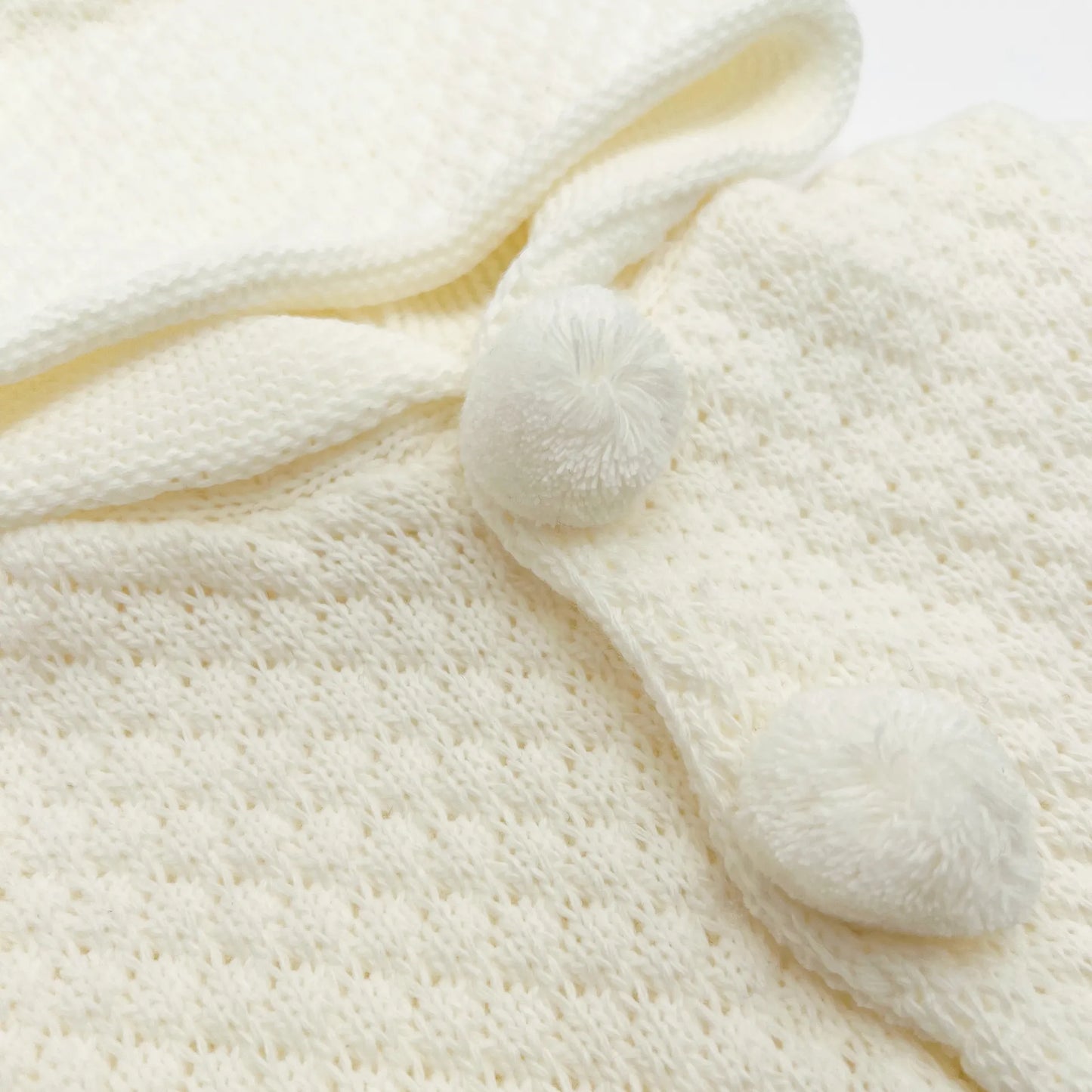 Detalle de chaqueta de punto con capucha y pompones en la zona de los botones perla