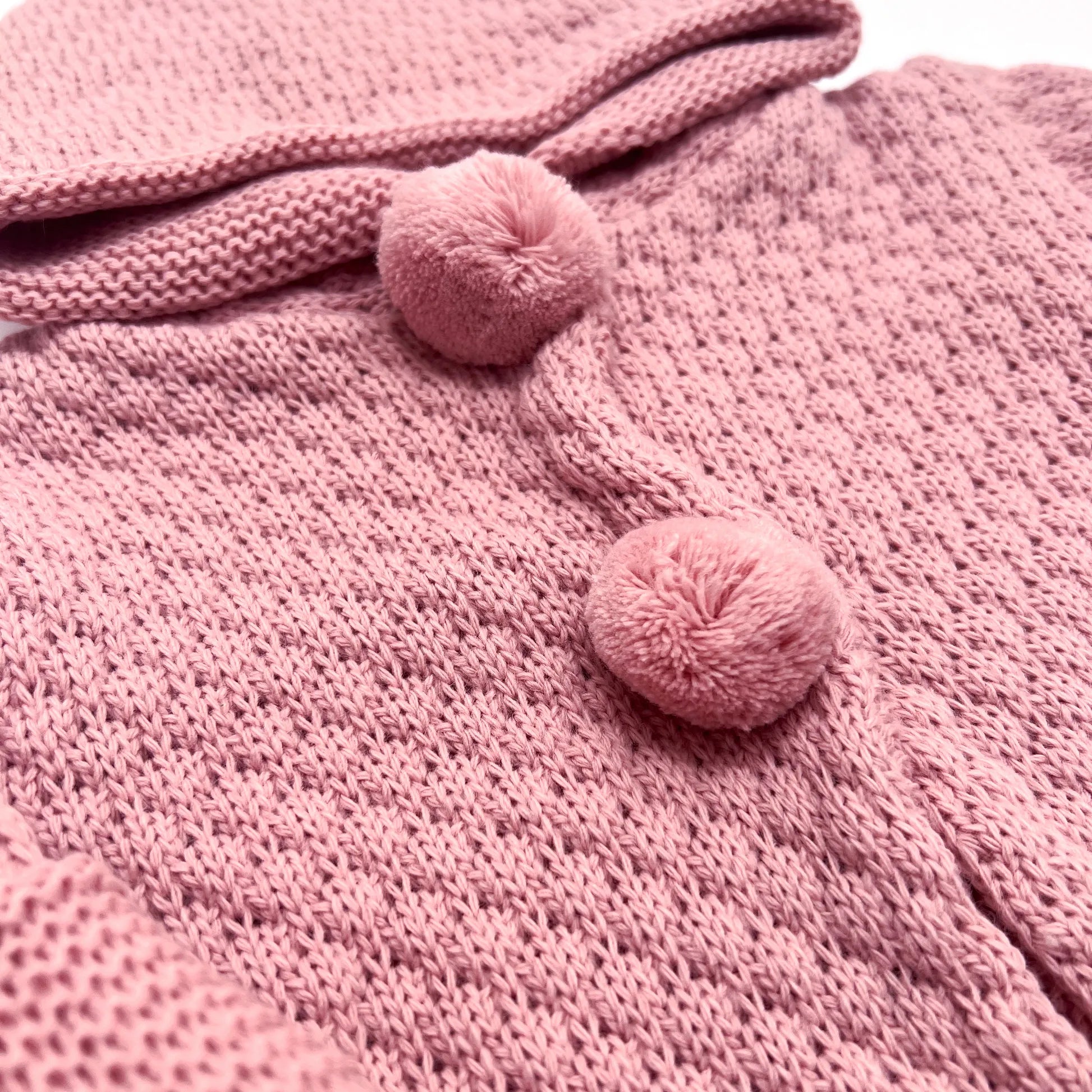 Detalle de chaqueta de punto con capucha y pompones en la zona de los botones rosa