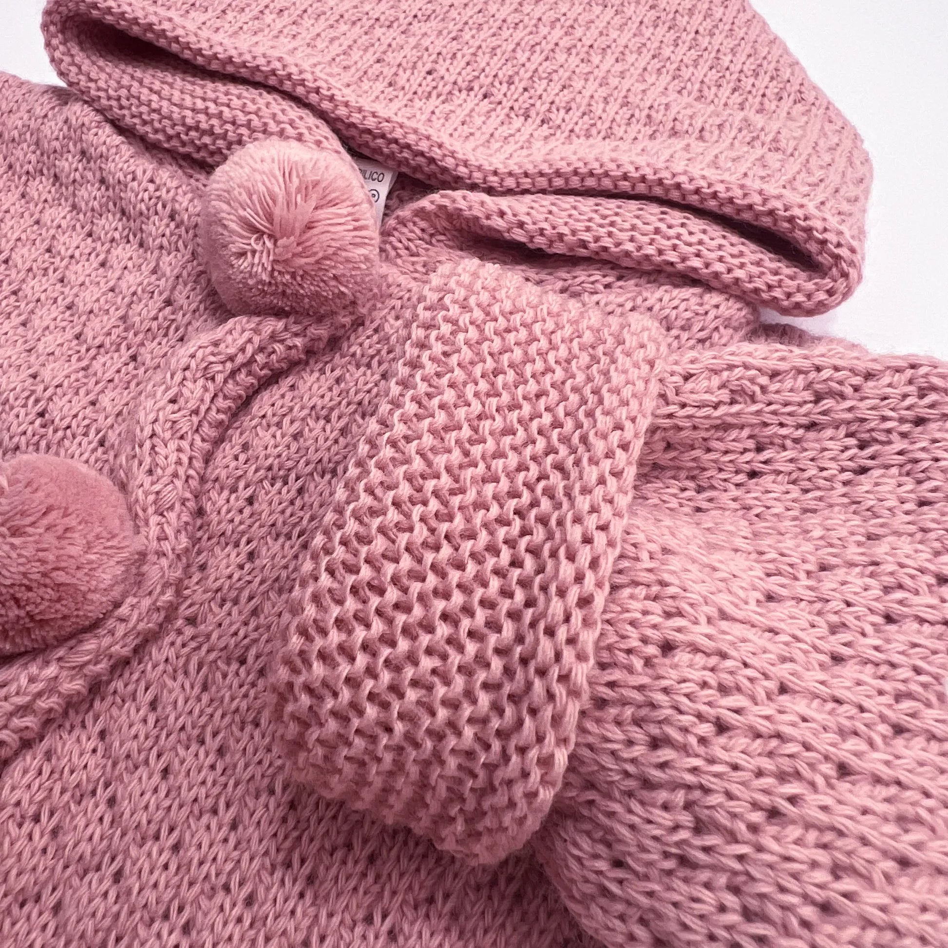 Detalle de chaqueta de punto con capucha y pompones en la zona de los botones rosa