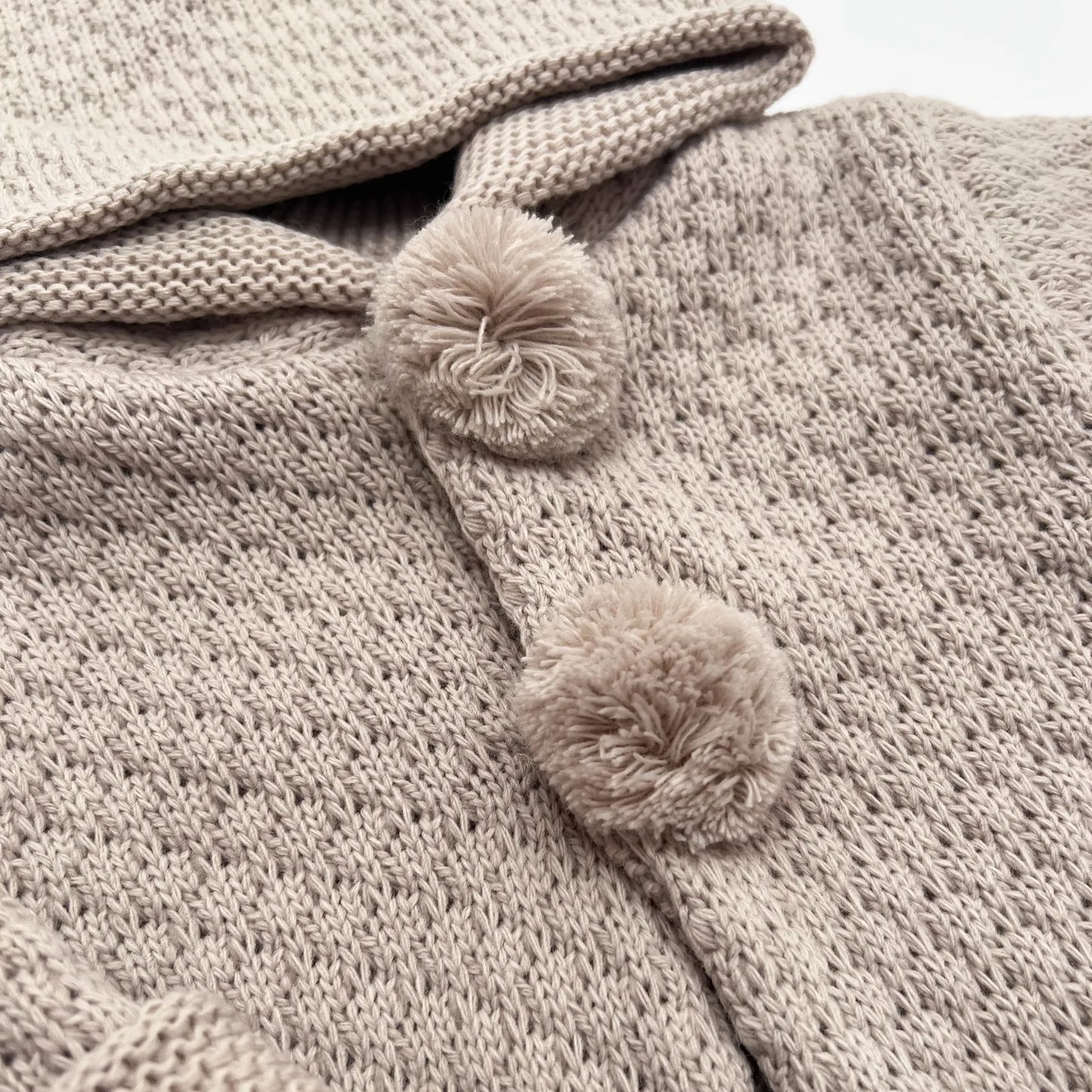 Detalle de chaqueta de punto con capucha y pompones en la zona de los botones topo