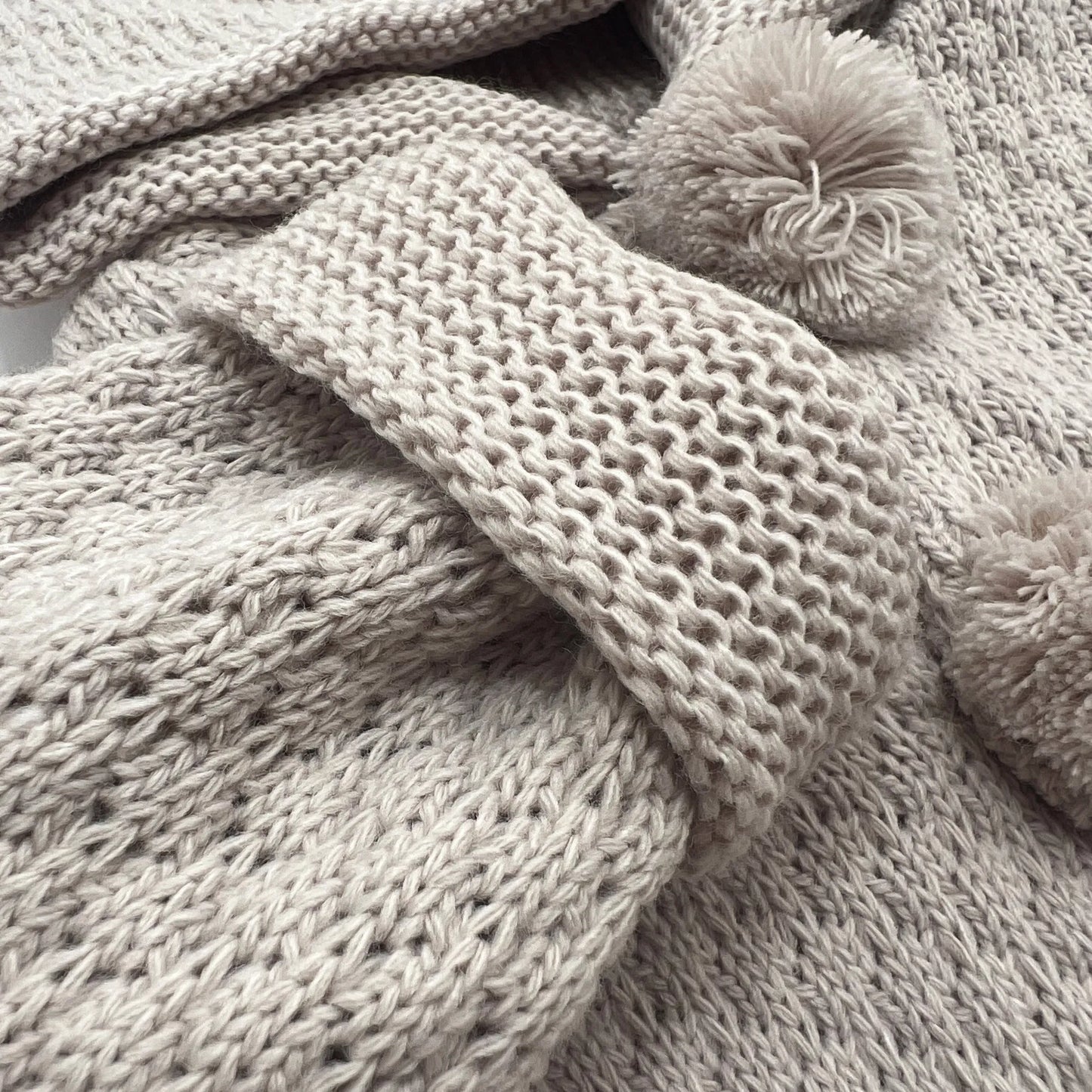 Detalle de chaqueta de punto con capucha y pompones en la zona de los botones topo
