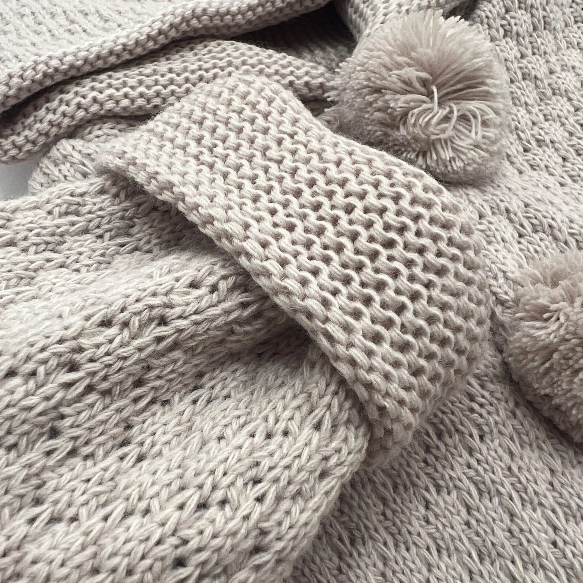 Detalle de chaqueta de punto con capucha y pompones en la zona de los botones topo
