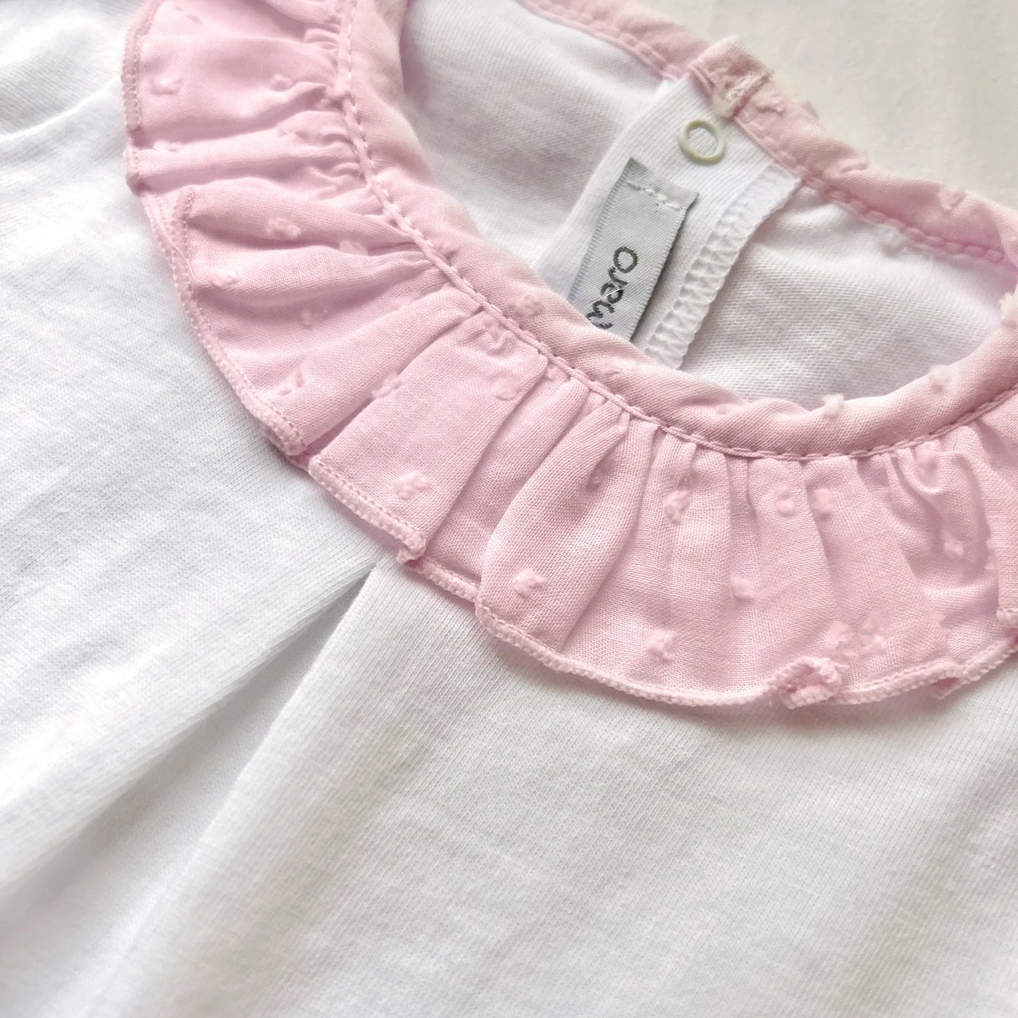Detalle de conjunto de niña de blusa con volante en el cuello y cubrepañal rosa