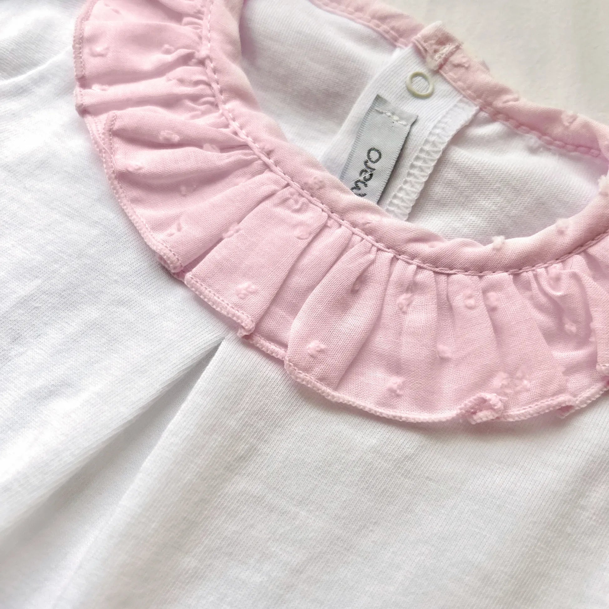 Detalle de conjunto de niña de blusa con volante en el cuello y cubrepañal rosa