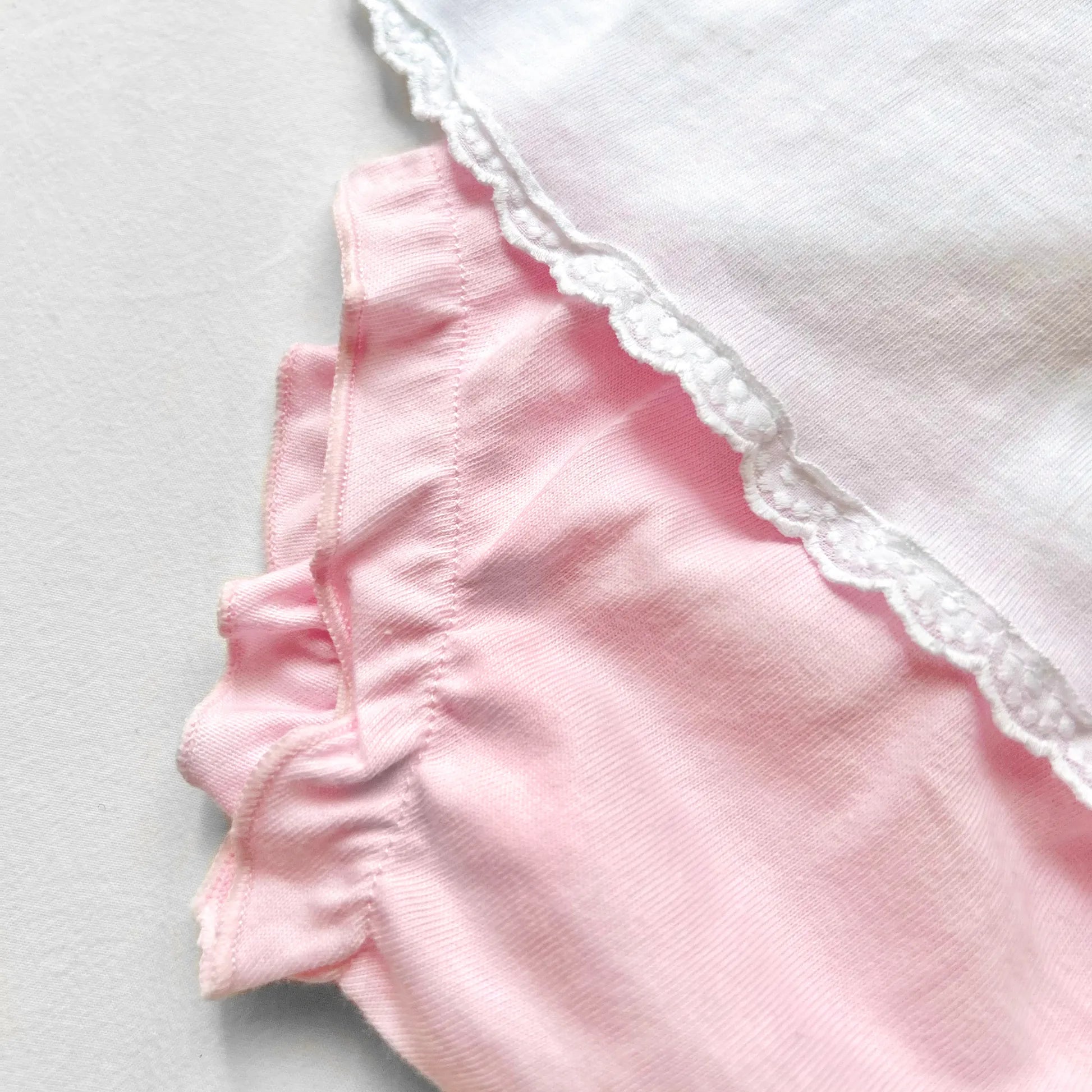 Detalle de conjunto de niña de blusa con volante en el cuello y cubrepañal rosa