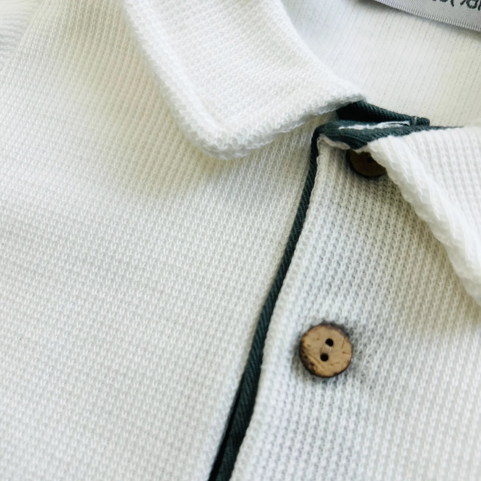 Detalle de conjunto de niño de camiseta color crudo con botones y pantalón corto de tela verde