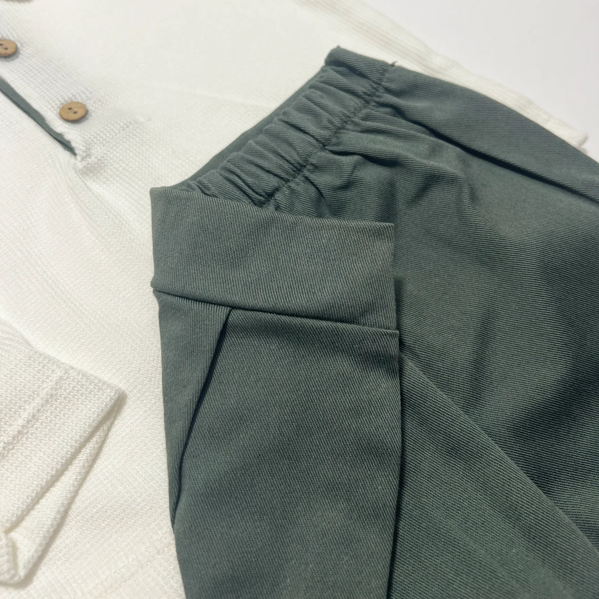 Detalle de conjunto de niño de camiseta color crudo con botones y pantalón corto de tela verde