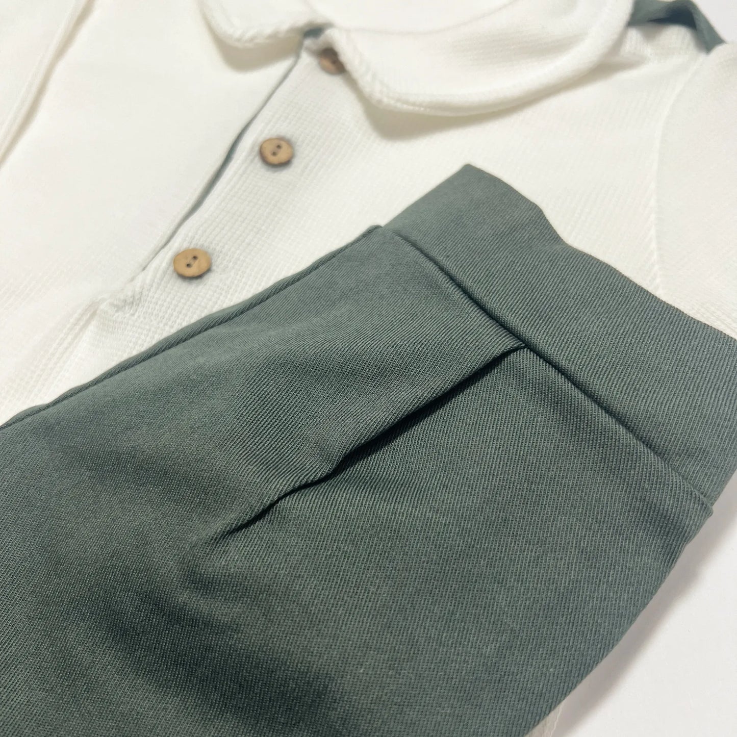 Detalle de conjunto de niño de camiseta color crudo con botones y pantalón corto de tela verde