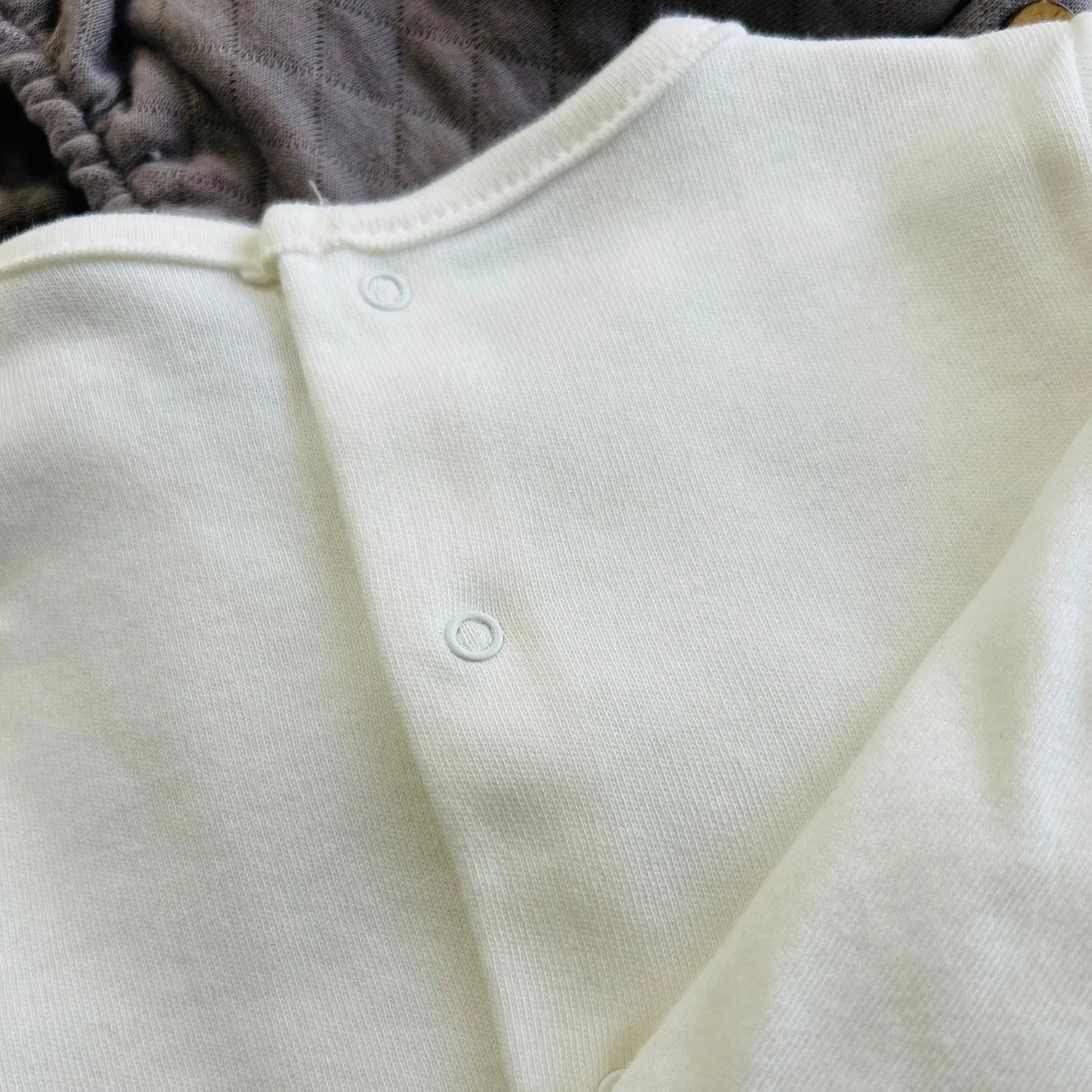 Detalle de conjunto de niño de camiseta blanca con faja decorativa y cubrepañal gris