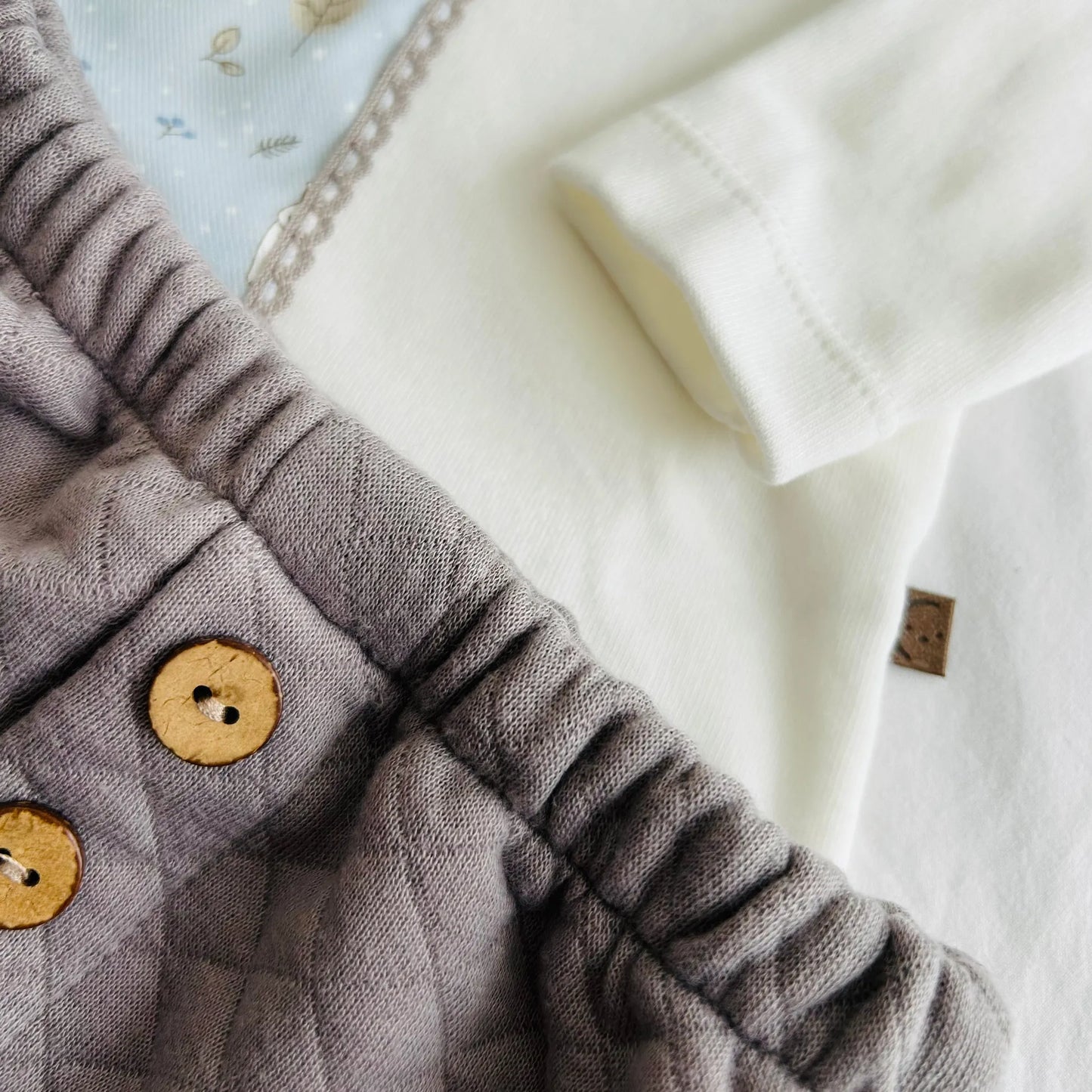 Detalle de conjunto de niño de camiseta blanca con faja decorativa y cubrepañal gris