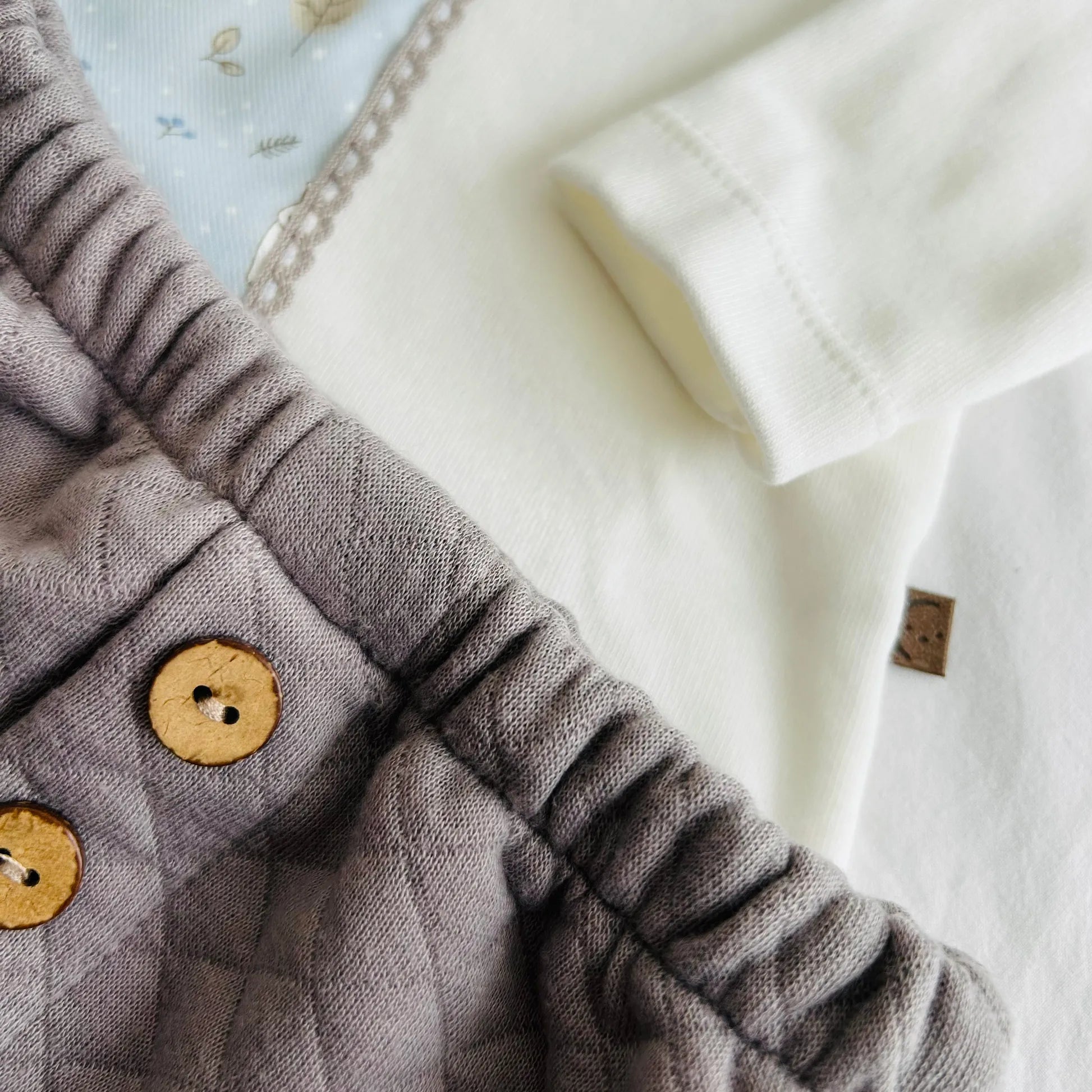 Detalle de conjunto de niño de camiseta blanca con faja decorativa y cubrepañal gris
