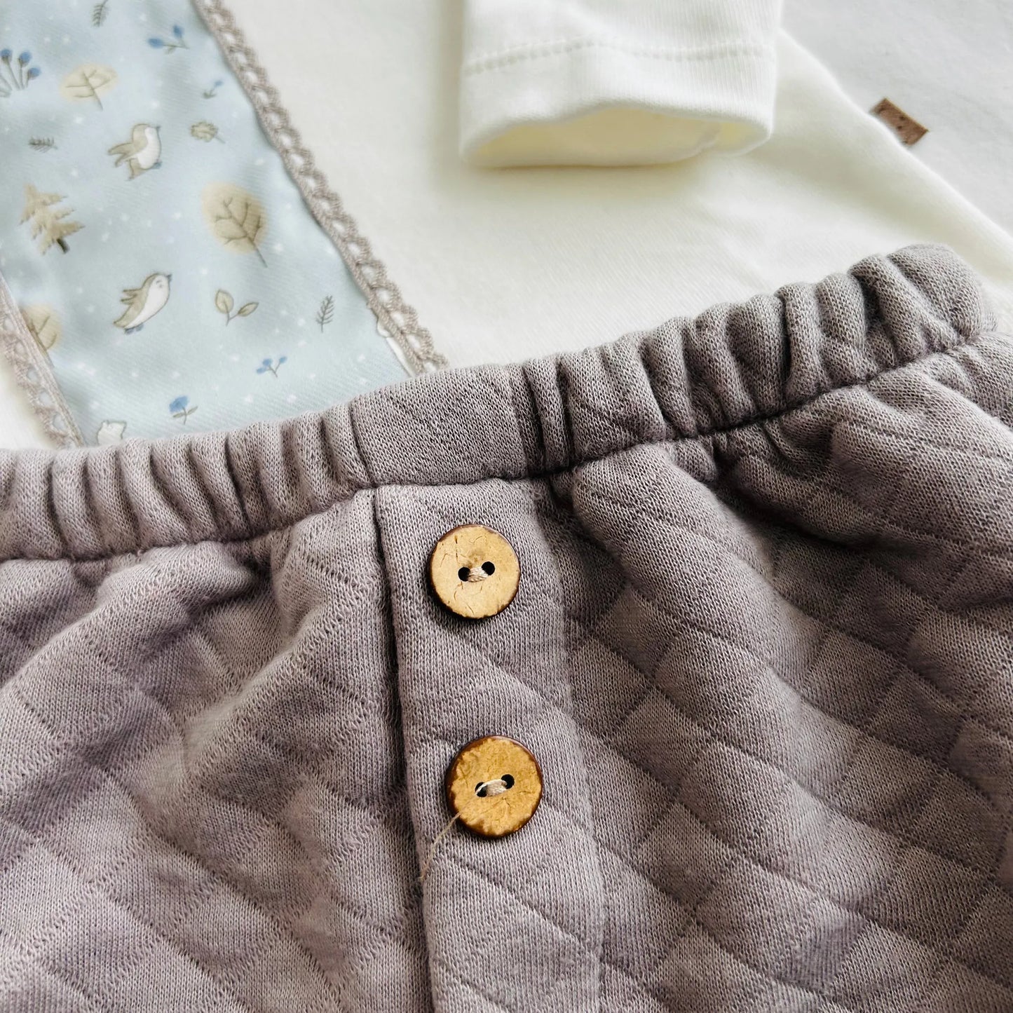 Detalle de conjunto de niño de camiseta blanca con faja decorativa y cubrepañal gris