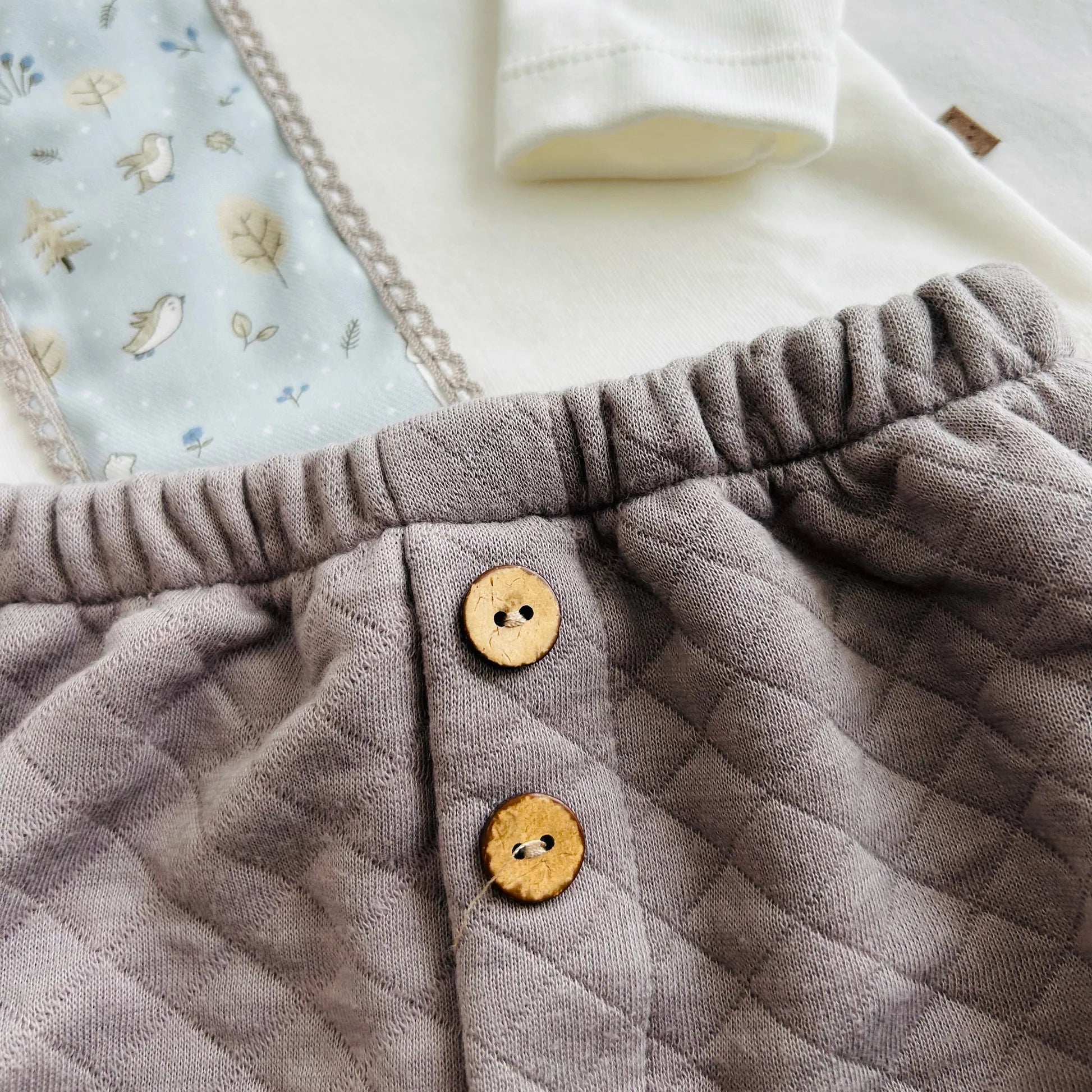 Detalle de conjunto de niño de camiseta blanca con faja decorativa y cubrepañal gris