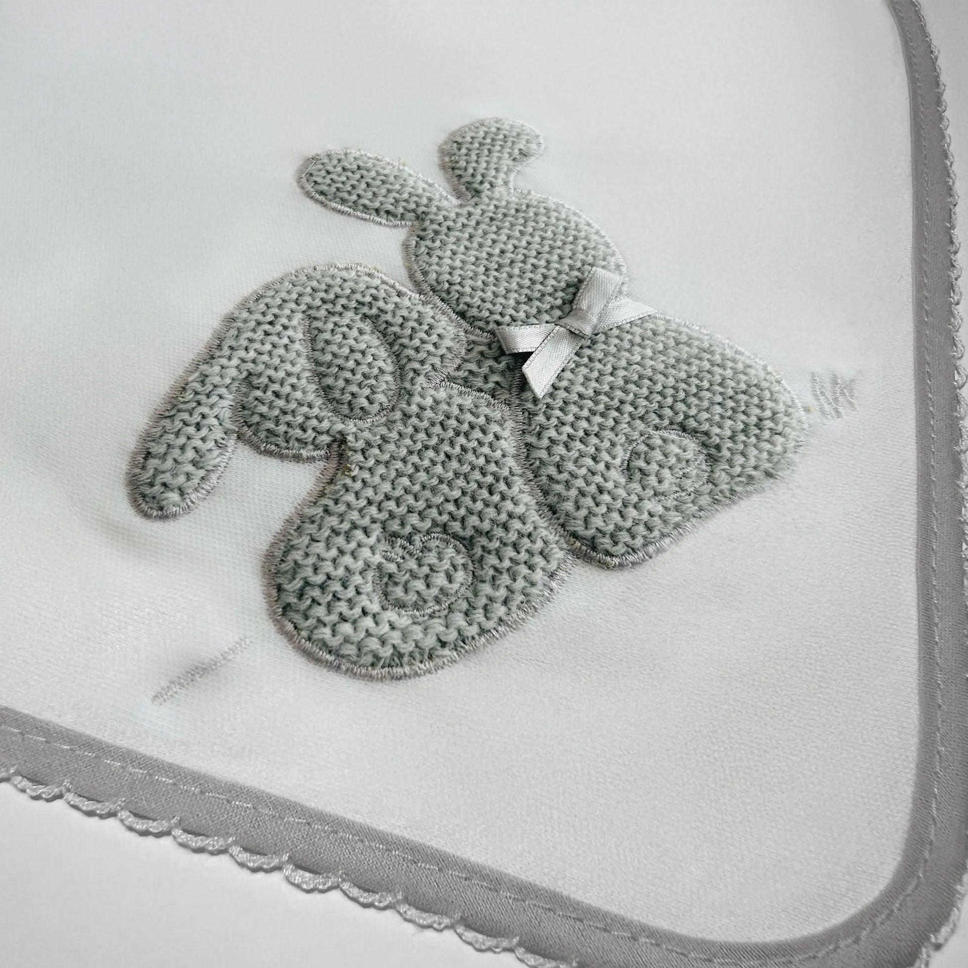 Detalle de paño para eructar con motivo de conejos de punto y lazito gris