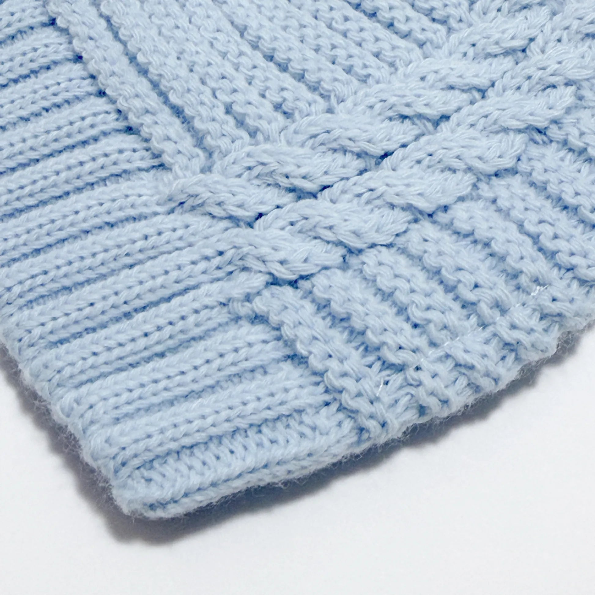 Detalle de gorro de punto trenzado con pompón azul