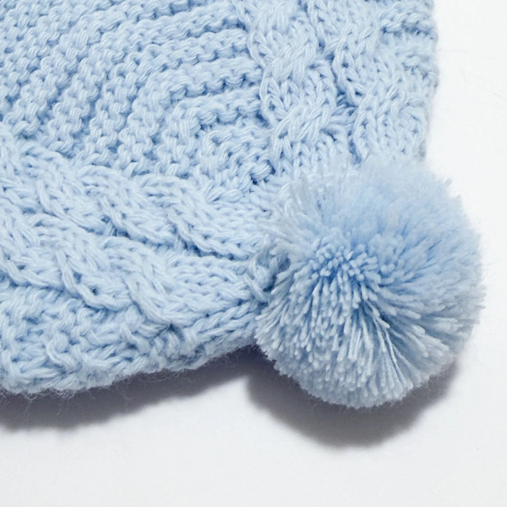 Detalle de gorro de punto trenzado con pompón azul