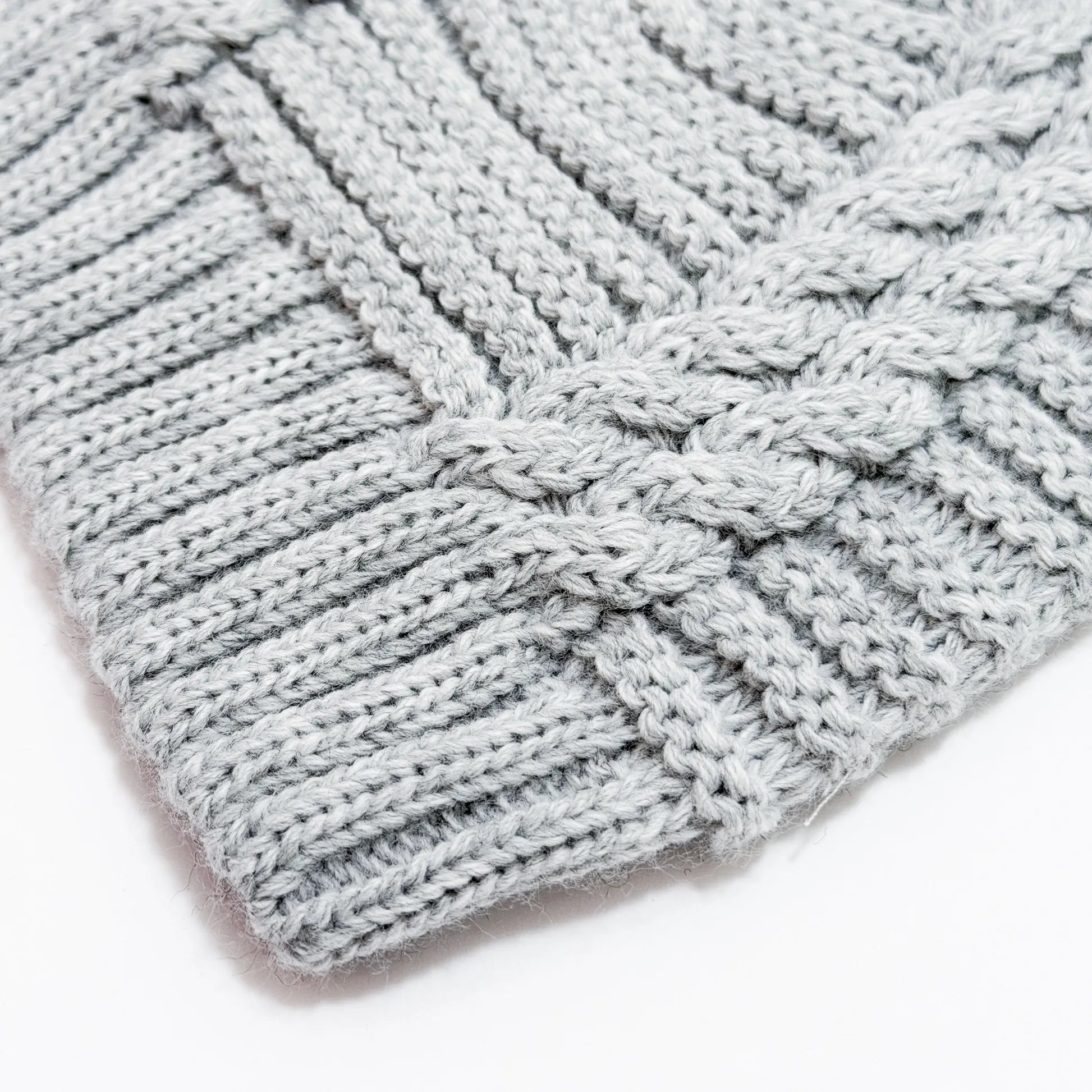 Detalle de gorro de punto trenzado con pompón gris