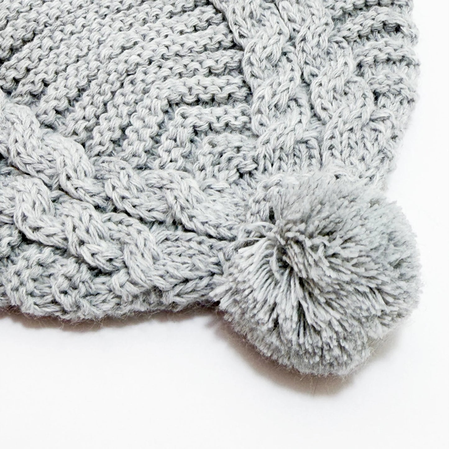 Detalle de gorro de punto trenzado con pompón gris