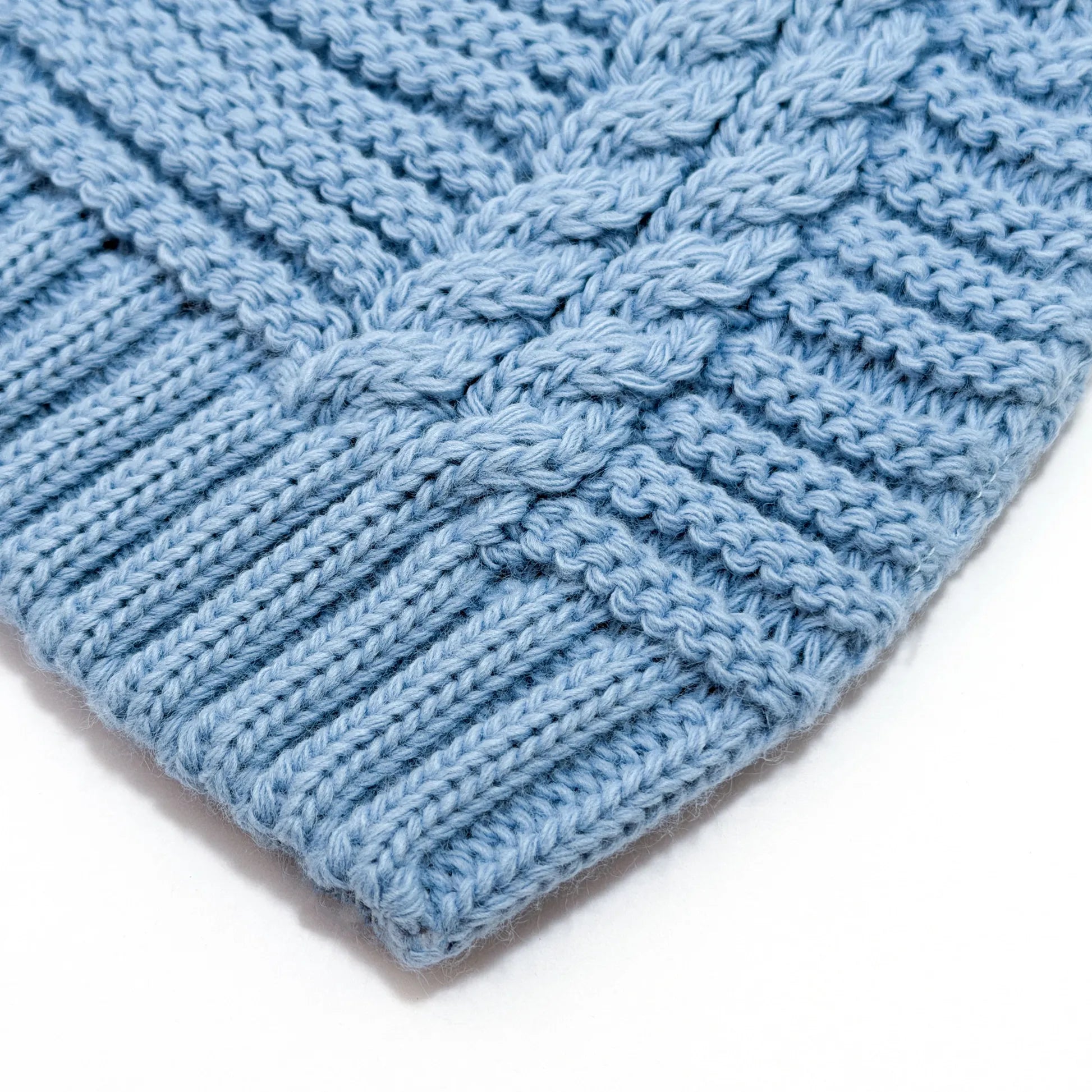 Detalle de gorro de punto trenzado con pompón cobalto
