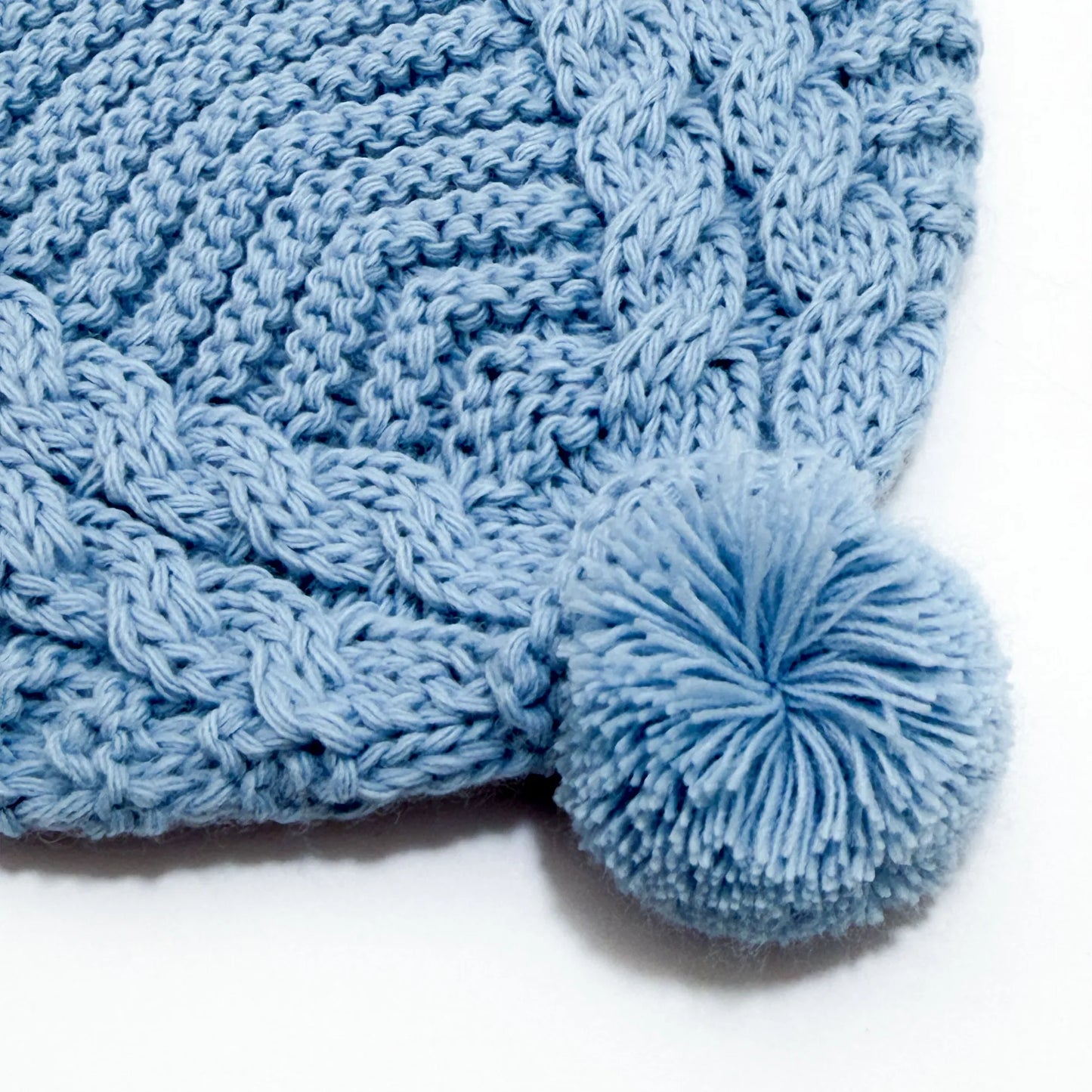 Detalle de gorro de punto trenzado con pompón cobalto