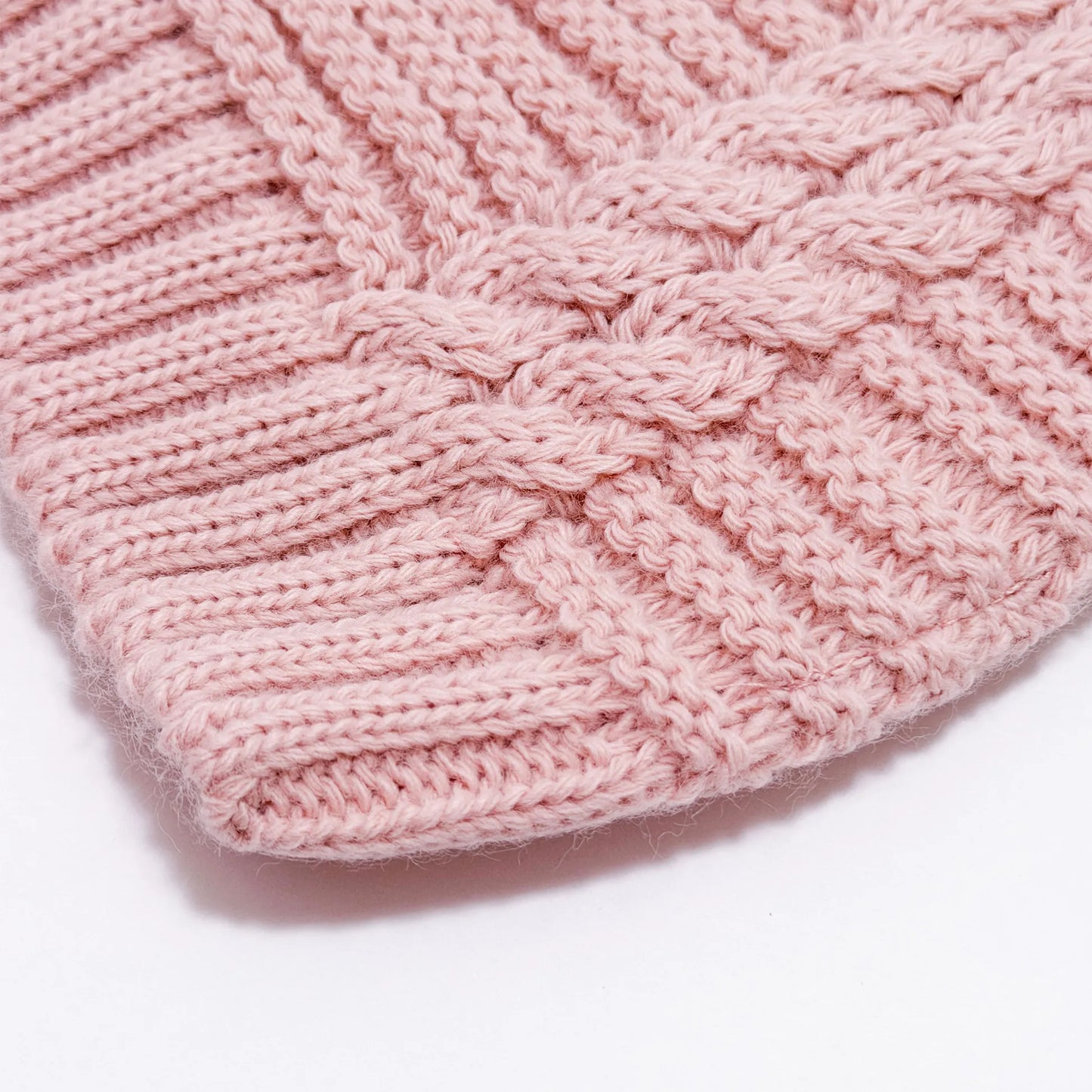 Detalle de gorro de punto trenzado con pompón rosa