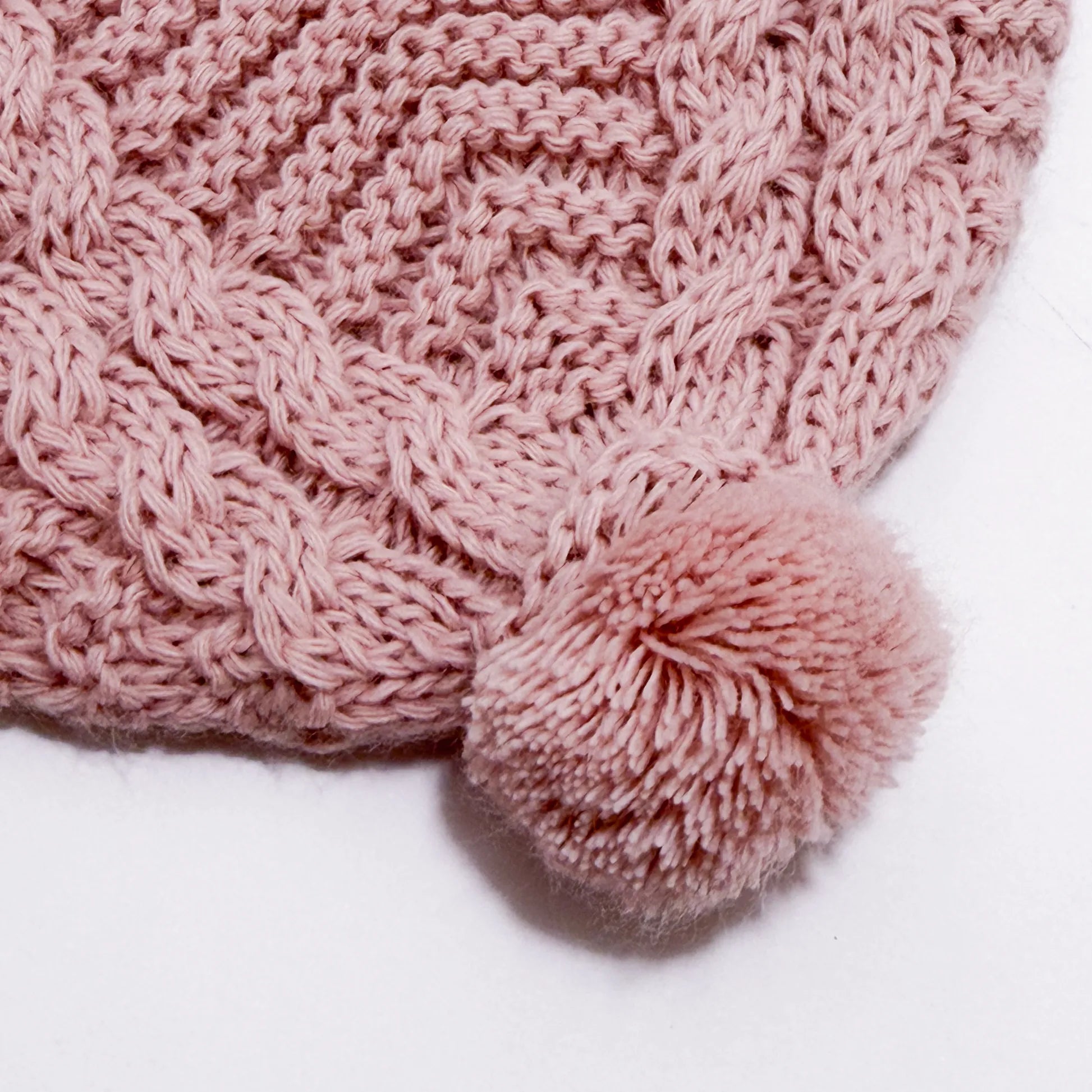 Detalle de gorro de punto trenzado con pompón rosa