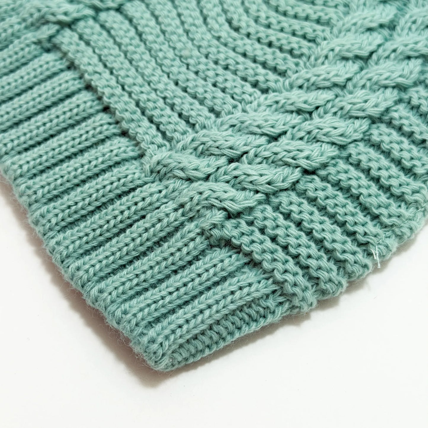 Detalle de gorro de punto trenzado con pompón verde