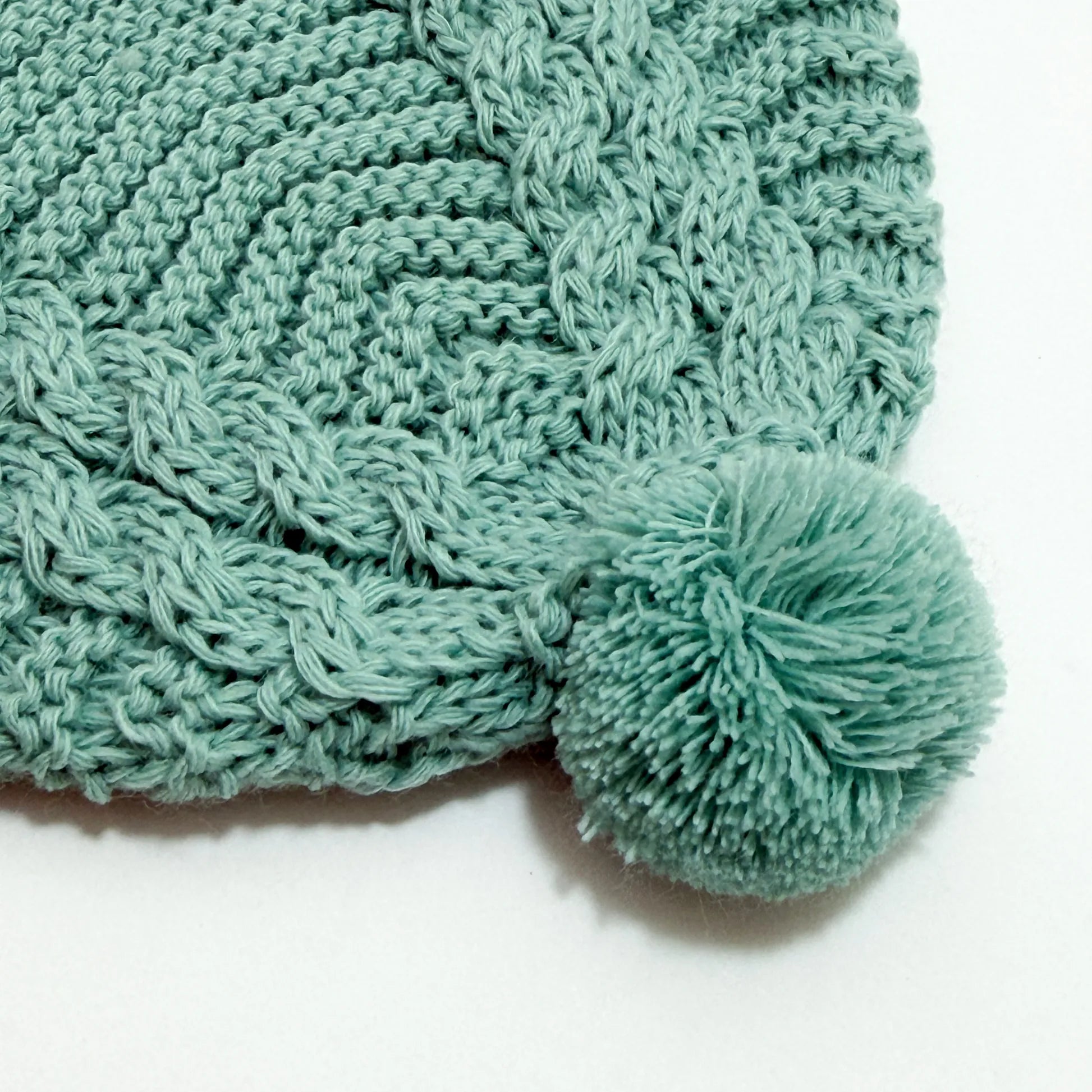 Detalle de gorro de punto trenzado con pompón verde