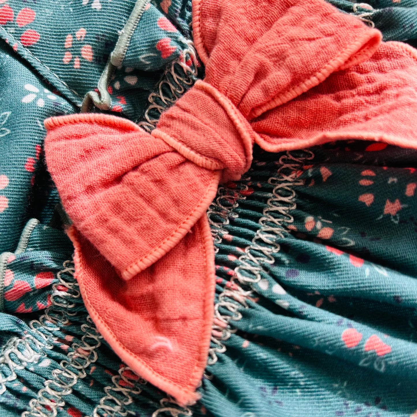 Detalle de peto de niña verde con estampado floral y lazo en el pecho coral en contraste