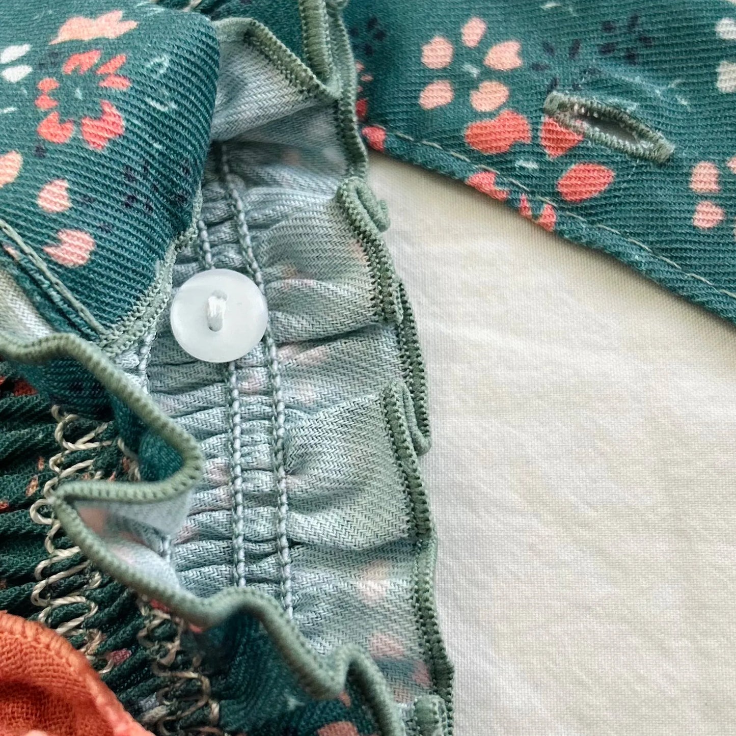 Detalle de peto de niña verde con estampado floral y lazo en el pecho coral en contraste