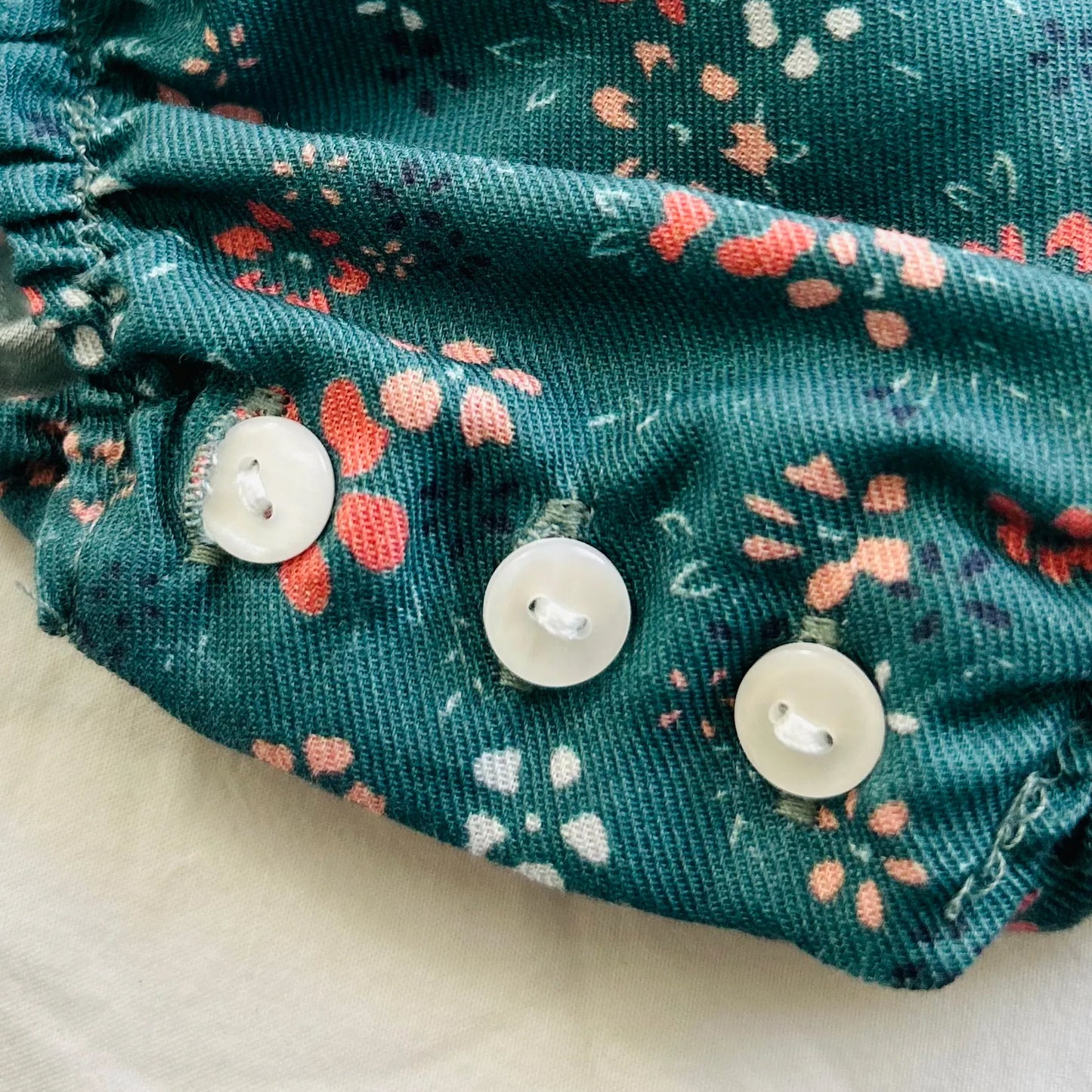 Detalle de peto de niña verde con estampado floral y lazo en el pecho coral en contraste
